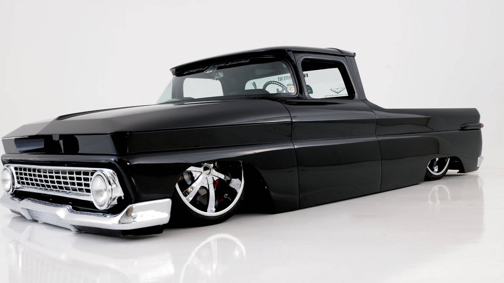 Lowrider 桌布 壁紙 — 一輛時尚的黑色經典低底盤皮卡車，配備鍍鉻輪圈和閃亮表面，放置在反射性白色攝影棚地板上。