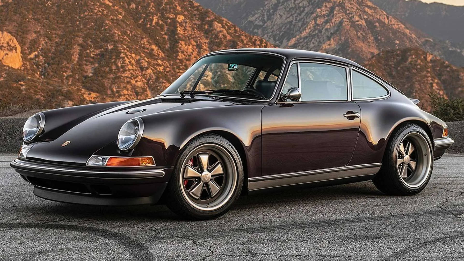 Singer 桌布 壁紙 — 一輛時尚的黑色經典保時捷911停在瀝青路上，背後是沐浴在金色日落光芒中的崎嶇山脈。