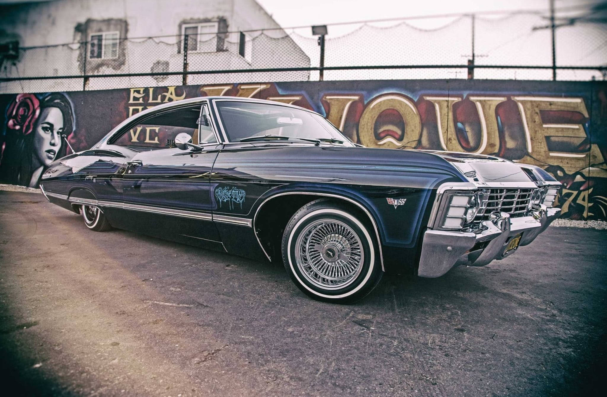 chevrolet impala 1967 桌布 壁紙 — 一輛時尚的黑色經典肌肉車，帶有鍍鉻細節，停在充滿活力的塗鴉牆前。