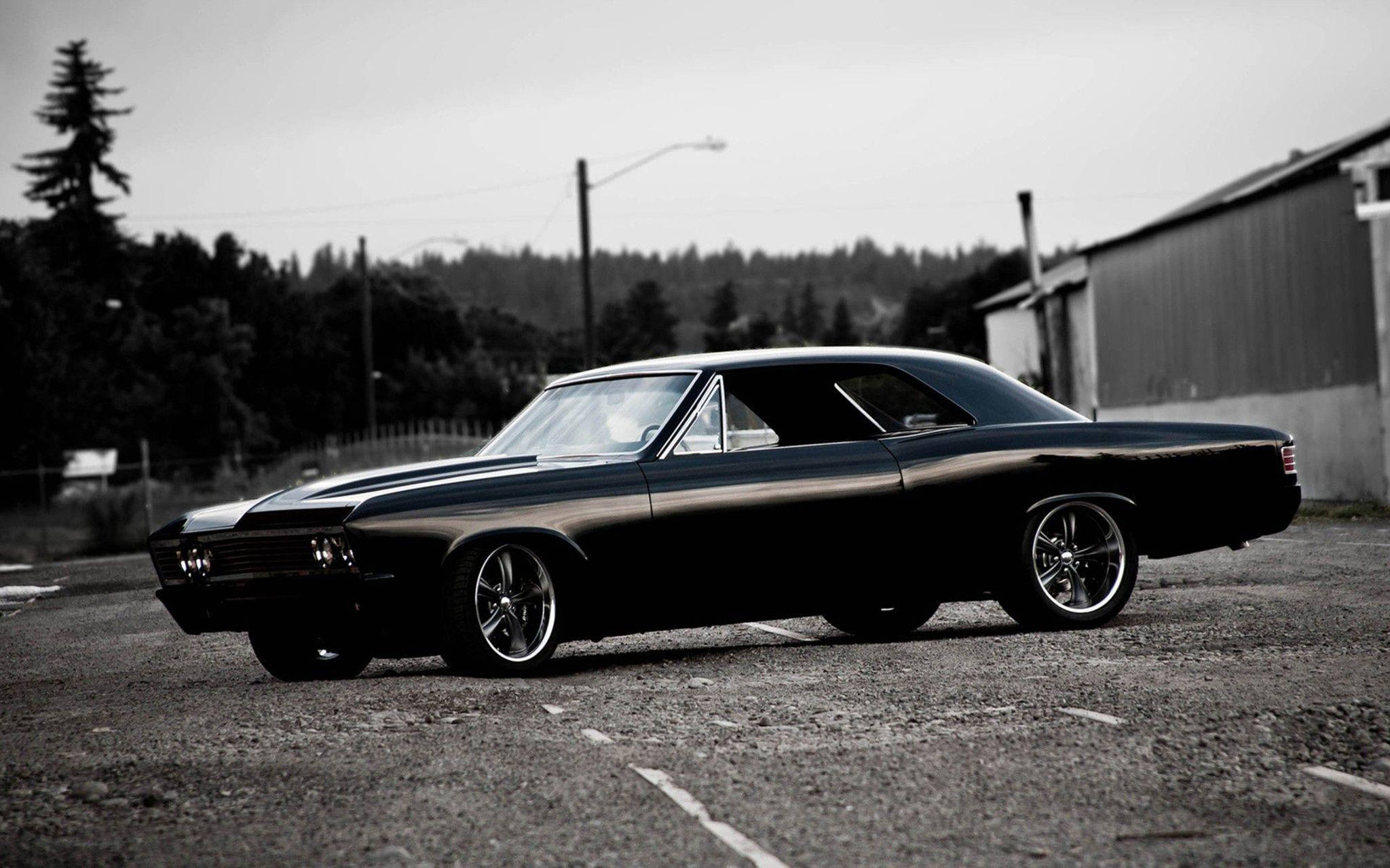 chevrolet impala 1967 桌布 壁紙 — 一輛時尚的黑色經典肌肉車，配備鍍鉻輪圈，停在單色工業環境的碎石地上。