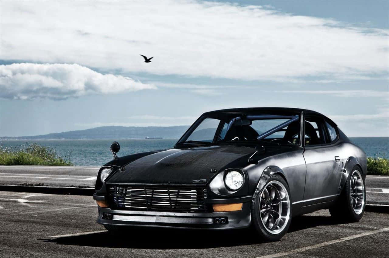 Datsun 桌布 壁紙 — 一輛時尚的黑色經典跑車停泊在海岸公路上，背景是海洋和陰天。