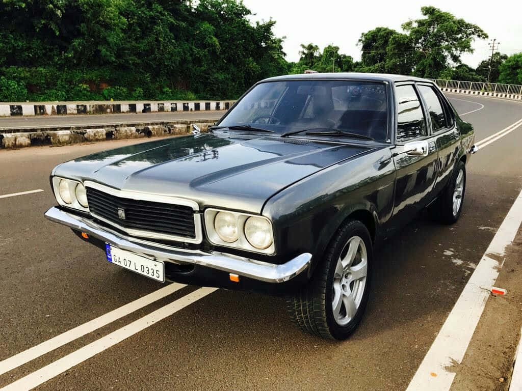 Hindustan Motors 桌布 壁紙 — 一輛時尚的黑色經典轎車停泊在彎曲的瀝青路上，旁邊是茂密的綠樹和混凝土護欄。