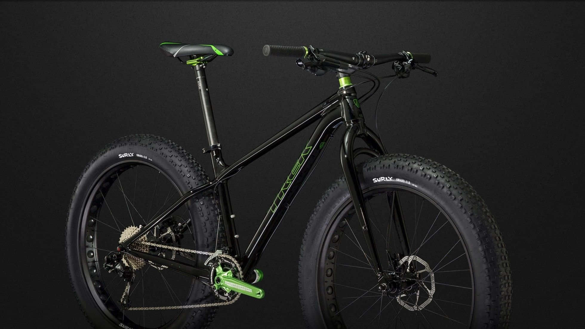 Bikes 桌布 壁紙 — 一輛時尚的黑色胖胎車帶有螢光綠色點綴，在黑暗的攝影棚背景下展示其堅固的輪胎和現代車架。