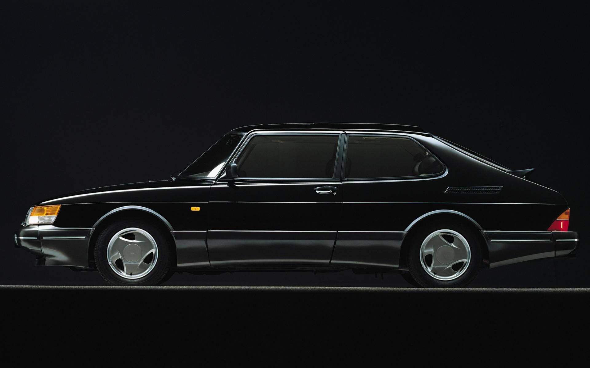 Saab 桌布 壁紙 — 一輛時尚的黑色薩博900 Turbo轎跑車在黑暗的攝影棚背景下以側面輪廓展示，配以戲劇性燈光。