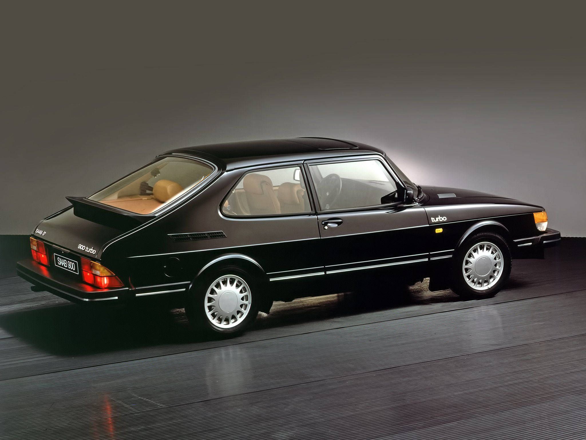 Saab 桌布 壁紙 — 一輛時尚的黑色薩博900 Turbo雙門轎跑車，配備米色內飾，在工作室中展示，帶有戲劇性燈光和反射地板。