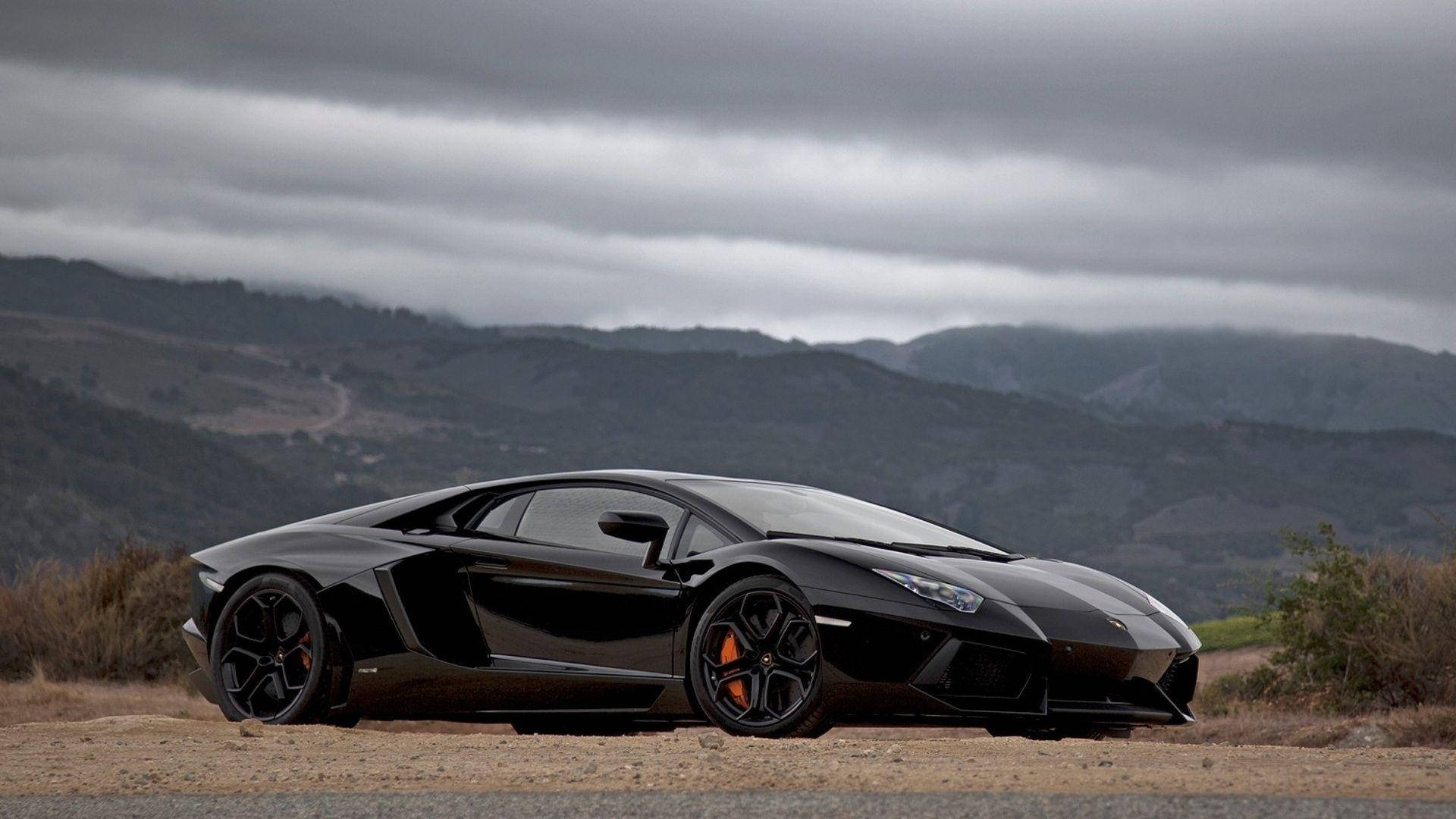 Lamborghini 4K 桌布 壁紙 — 一輛時尚的黑色藍寶堅尼 Aventador 停在泥土路上，背景是起伏的丘陵和陰天。