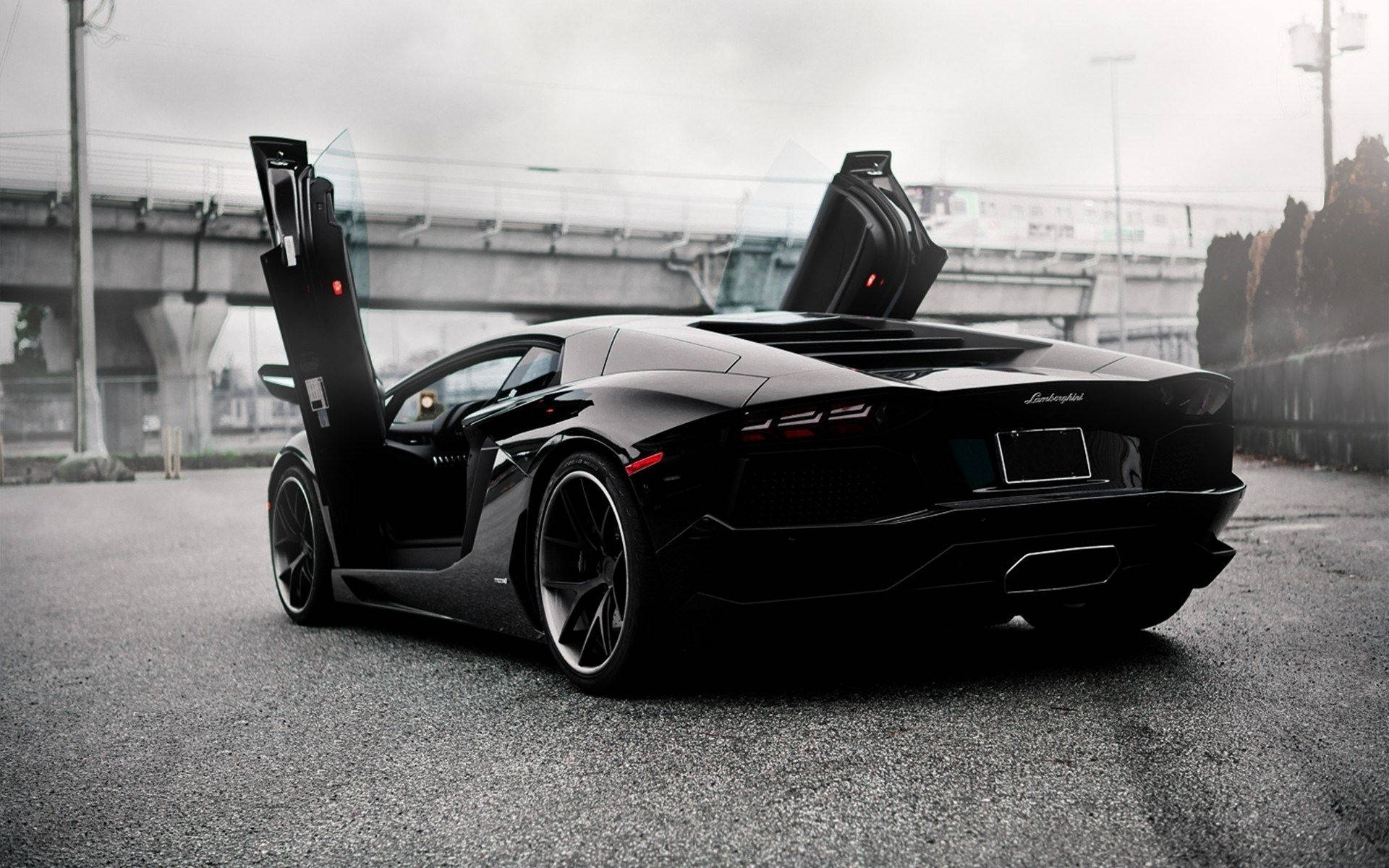 跑車 桌布 壁紙 — 一輛時尚的黑色藍寶堅尼 Aventador 打開鷗翼車門，停在灰色天橋下的柏油路上。