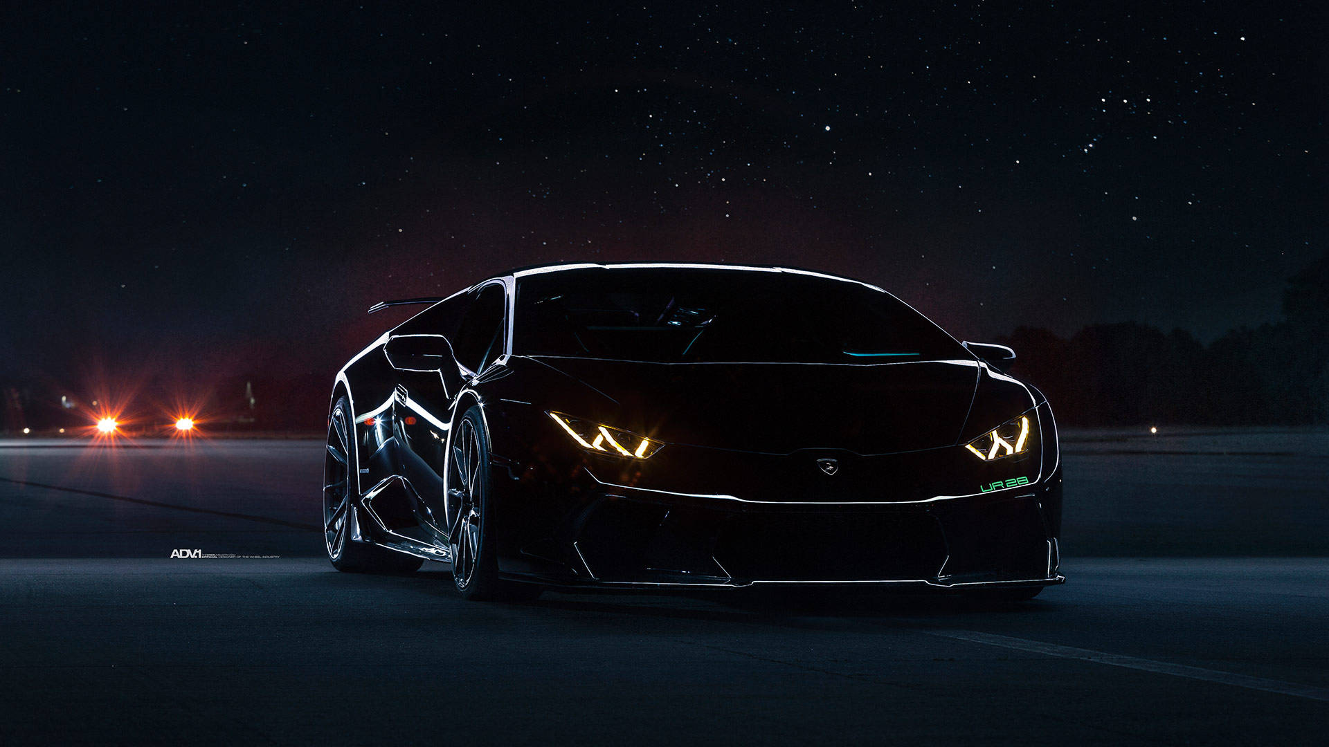 Lamborghini 4K 桌布 壁紙 — 一輛時尚的黑色藍寶堅尼 Huracán 在星空下，於空曠的道路上閃耀著發光的車頭燈。