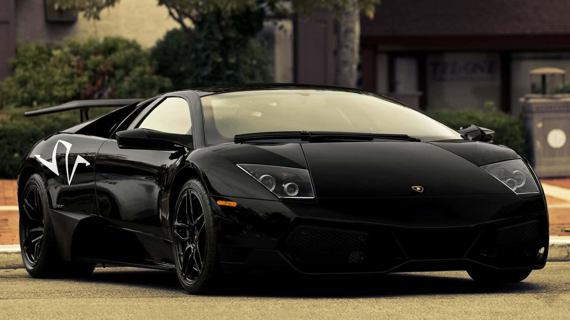Lamborghini Murciélago 桌布 壁紙 — 一輛時尚的黑色藍寶堅尼 Murciélago 停放在街道上，背景有樹木和建築物。