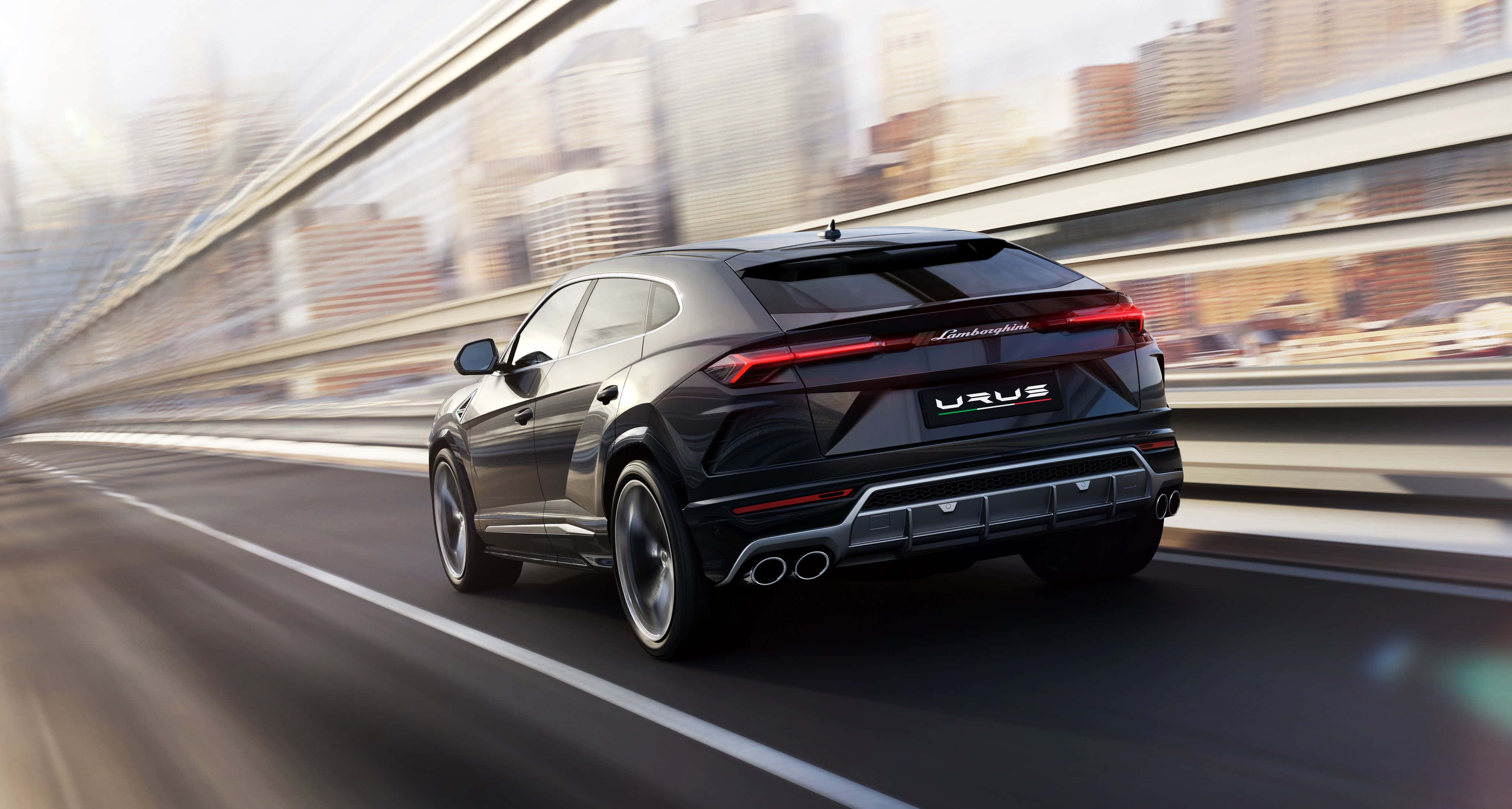 Lamborghini Urus 桌布 壁紙 — 一輛時尚的黑色藍寶堅尼 Urus 在高速公路上疾馳，背景是模糊的城市天際線。