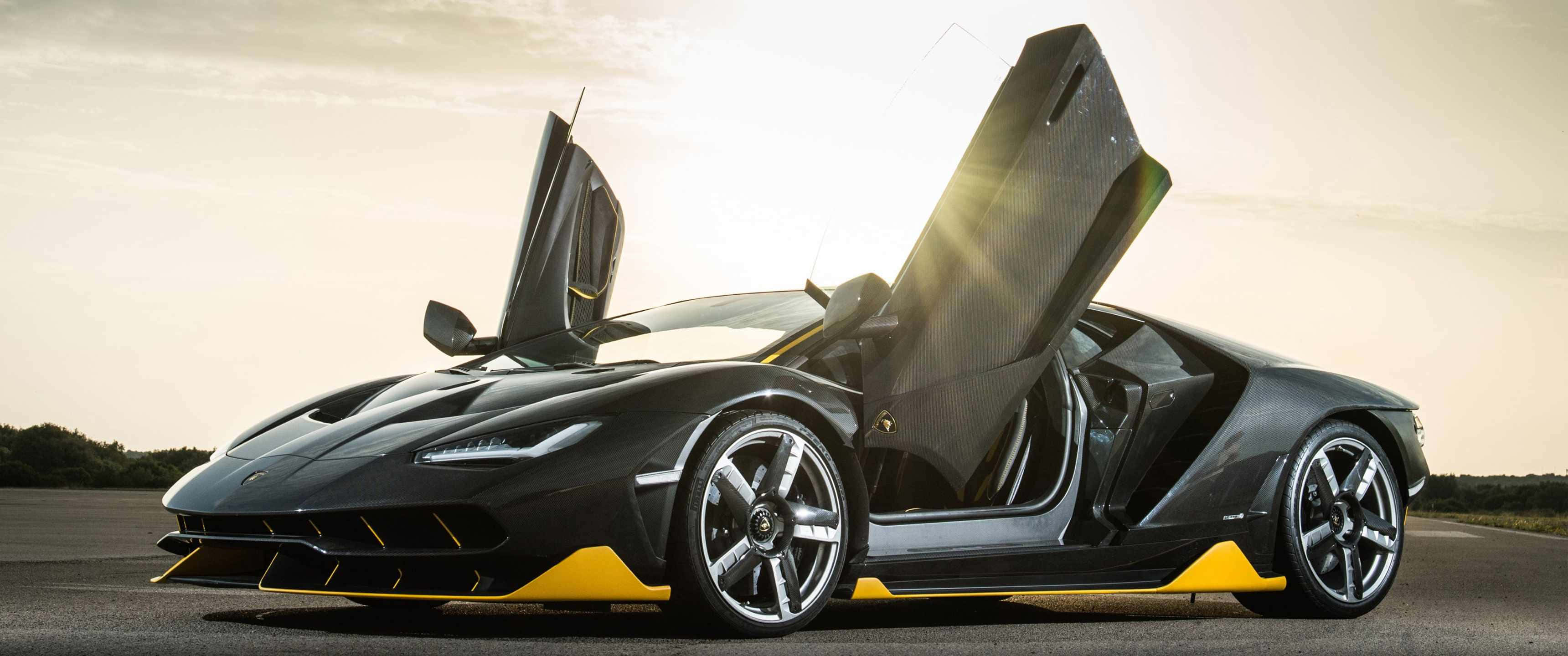 3440x1440p Lamborghini 桌布 壁紙 — 一輛時尚的黑色藍寶堅尼，帶有黃色點綴和剪刀門，在金色夕陽天空下敞開。
