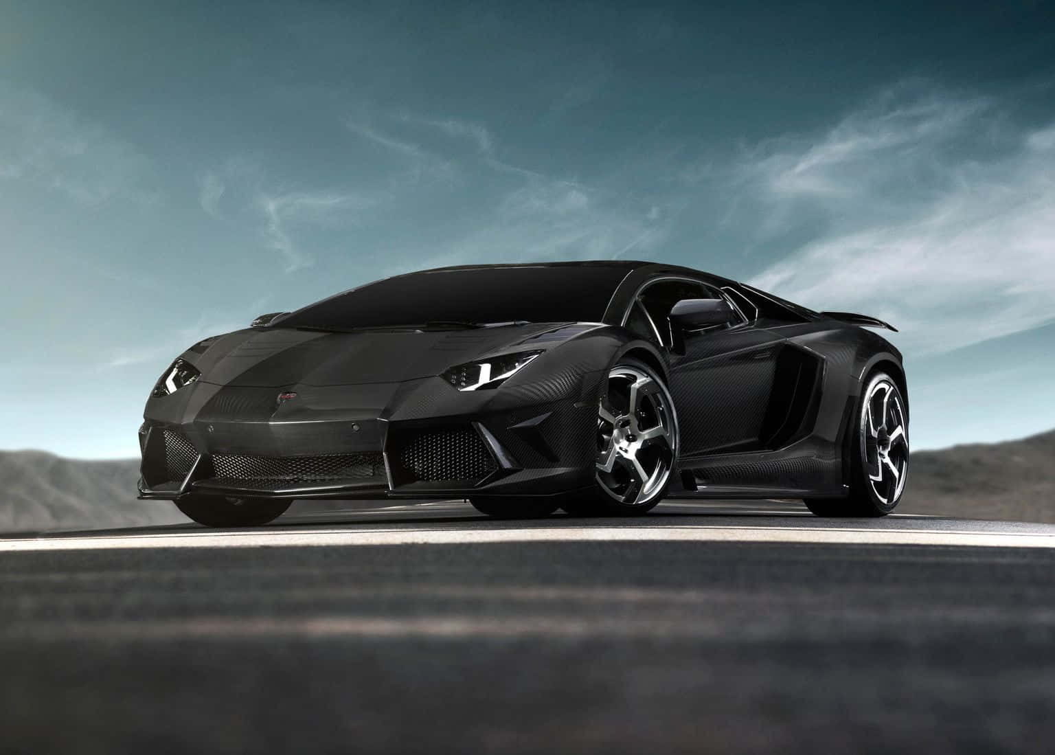 Luxury 桌布 壁紙 — 一輛時尚的黑色藍寶堅尼Aventador跑車，帶有碳纖維細節，在陰沉天空下的沙漠道路上蓄勢待發。