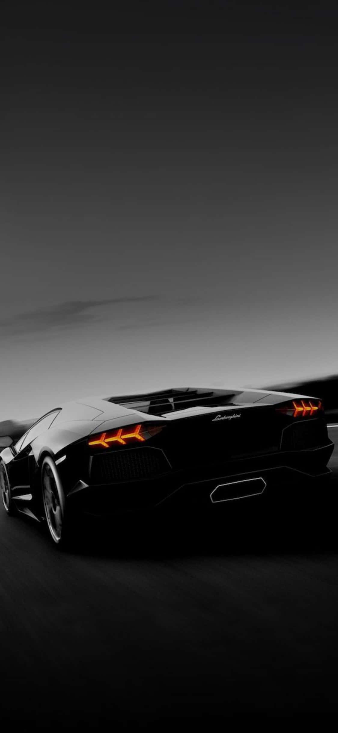 iPhone X Lamborghini 桌布 壁紙 — 一輛時尚的黑色藍寶堅尼Aventador在黃昏時分疾馳而去，橙色尾燈在深色漸變天空下閃閃發光。