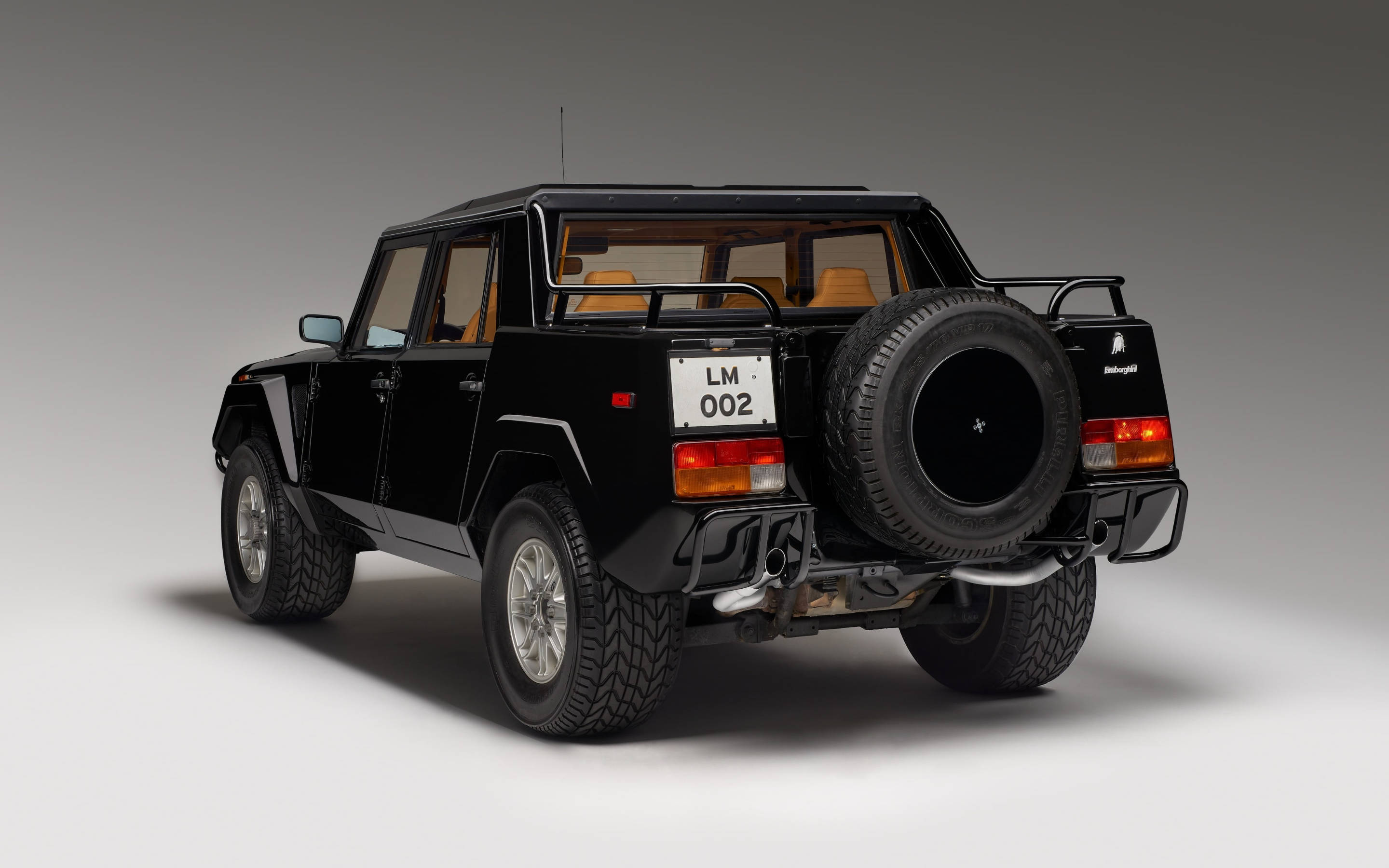 lambo 桌布 壁紙 — 一輛時尚的黑色藍寶堅尼LM002 SUV，後方裝有備用輪胎，在攝影棚環境中從後方斜側四分之三角度拍攝。