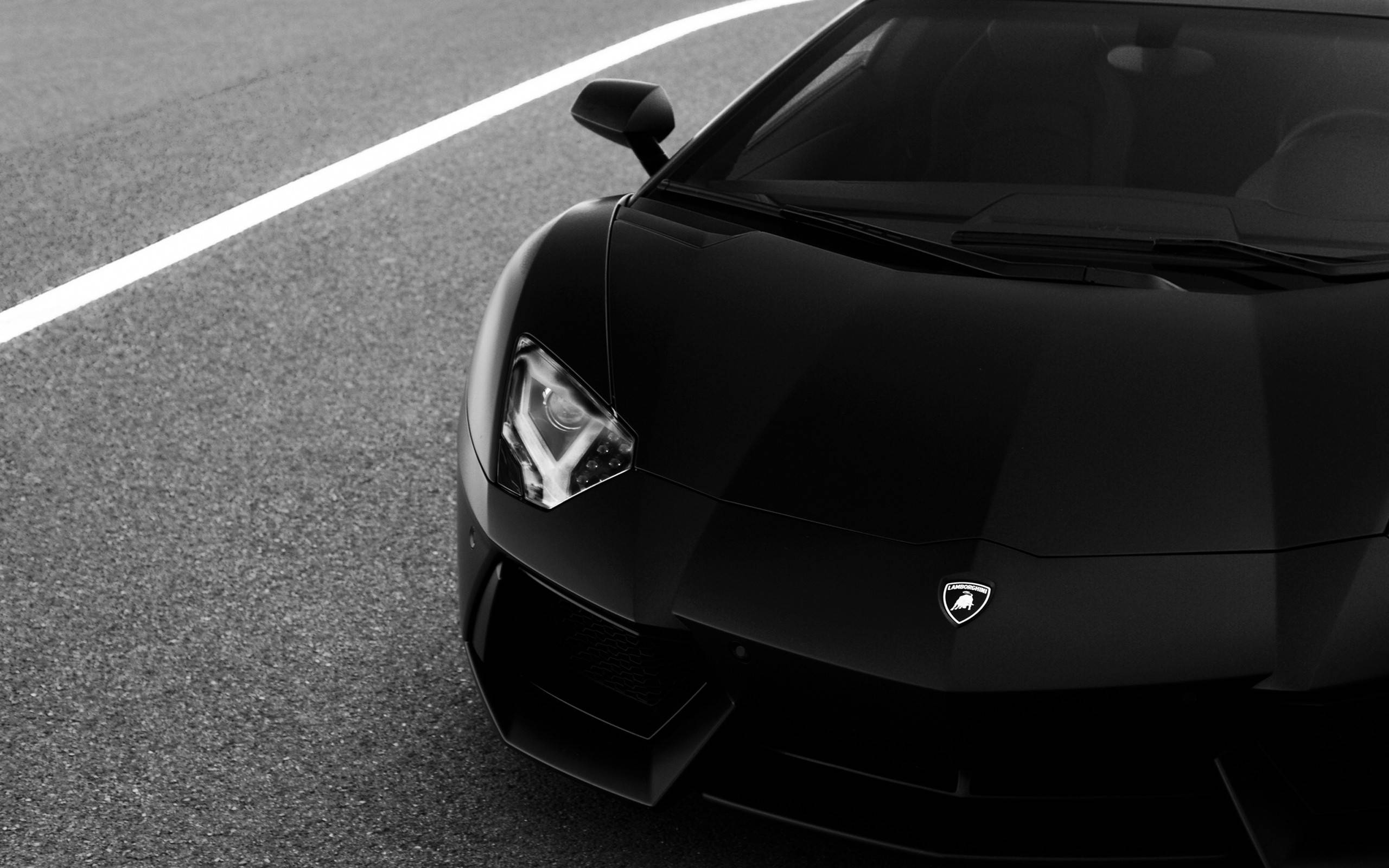 Lamborghini 4K 桌布 壁紙 — 一輛時尚的黑色藍寶堅尼跑車停在有白色線的柏油路上。