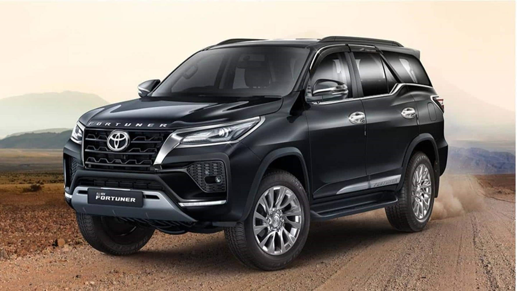 Toyota 桌布 壁紙 — 一輛時尚的黑色豐田 Fortuner SUV 在塵土飛揚的沙漠景觀中強勁行駛，遠山在朦朧的天空下若隱若現。