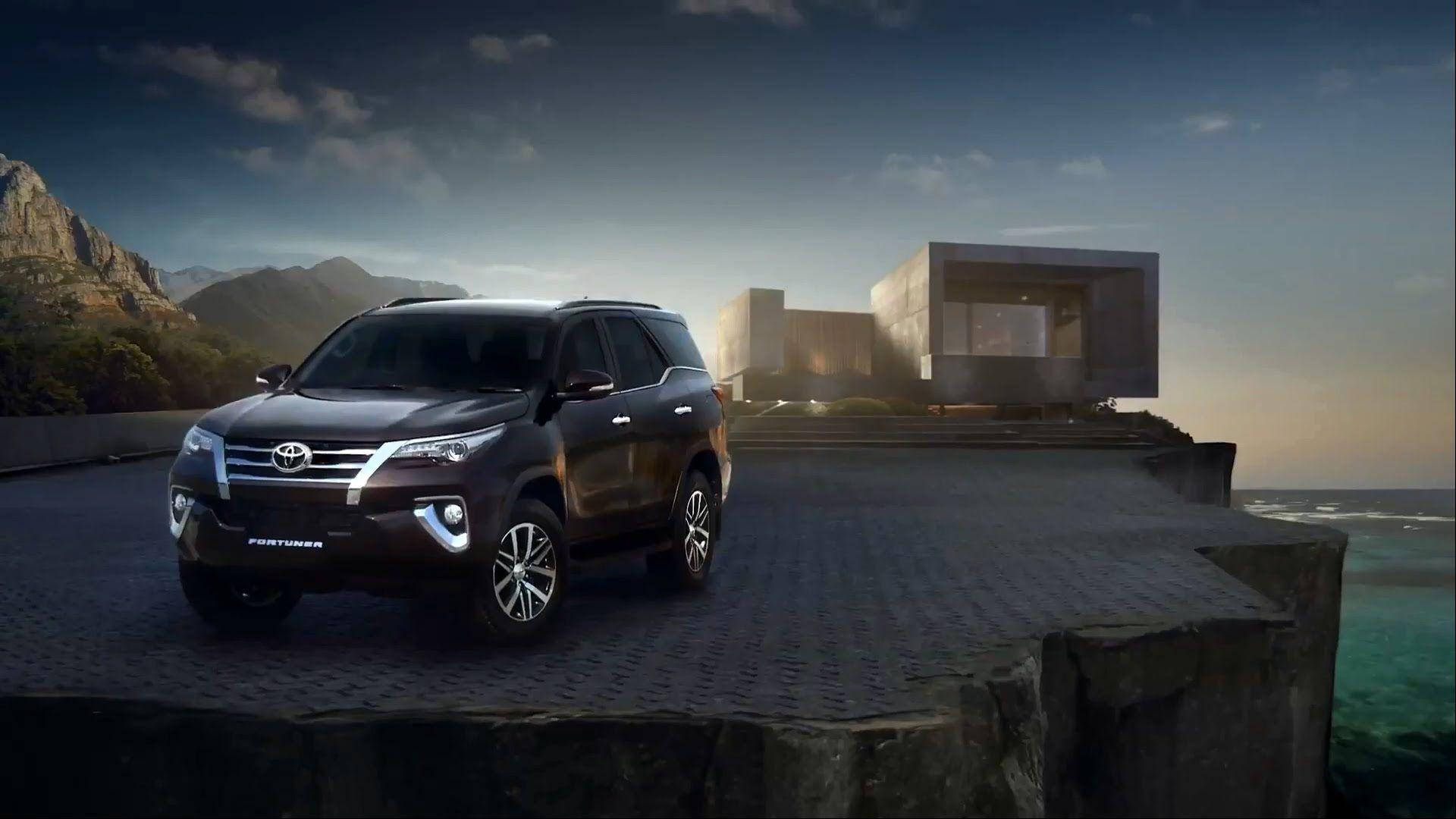 Toyota 桌布 壁紙 — 一輛時尚的黑色豐田 Fortuner SUV 停在懸崖邊的車道上，旁邊是一棟現代房屋，背景是黃昏時的海洋和山脈。