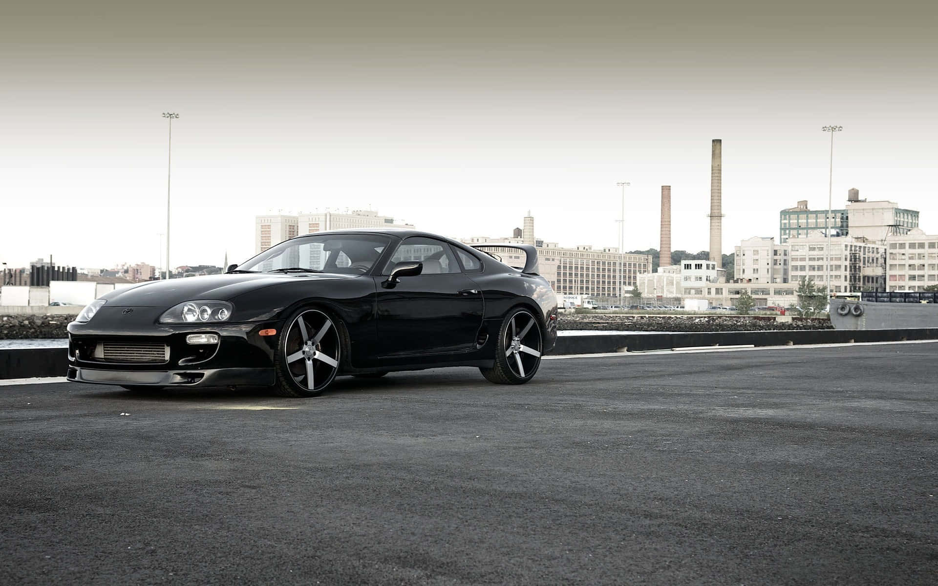 黑色豐田Supra停放在城市工業區，背景有城市建築。 — Toyota Supra Mk4 壁紙
