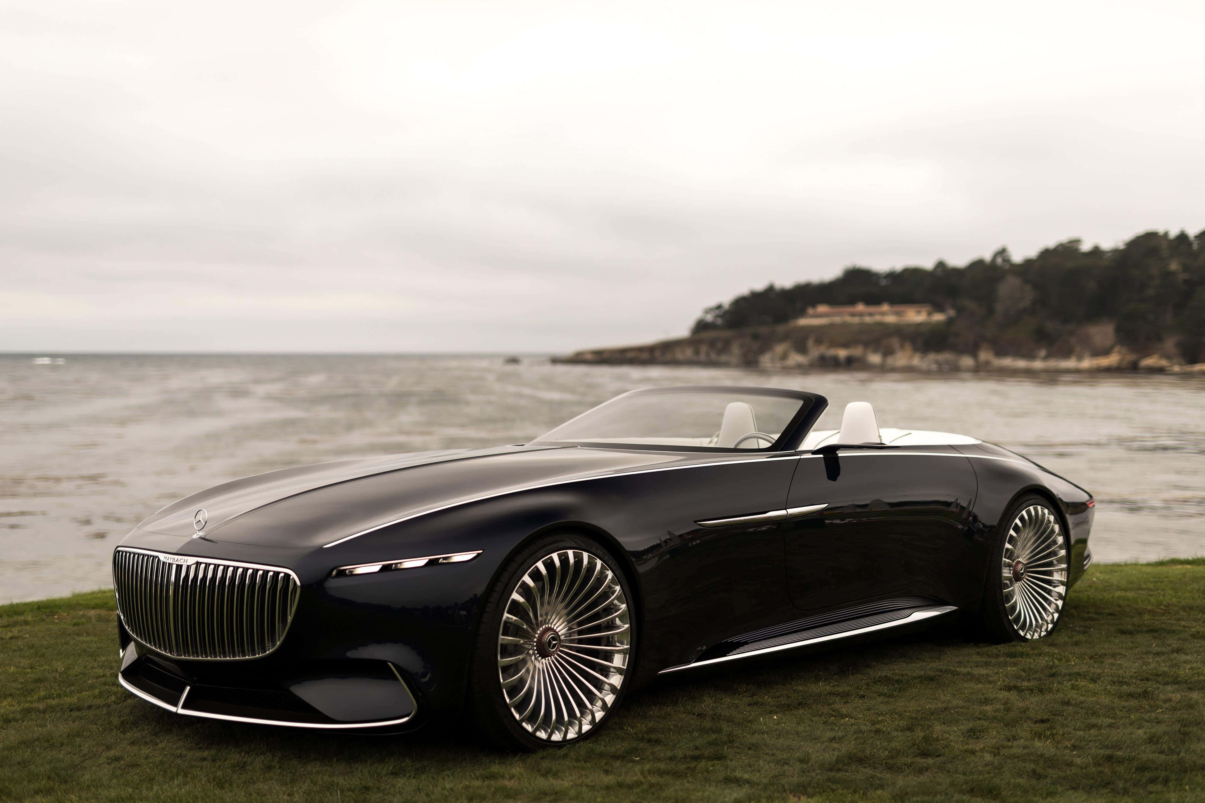 Maybach 桌布 壁紙 — 一輛時尚的黑色豪華敞篷車配銀色輪圈，停放在平靜海洋旁的草地上，天空多雲。