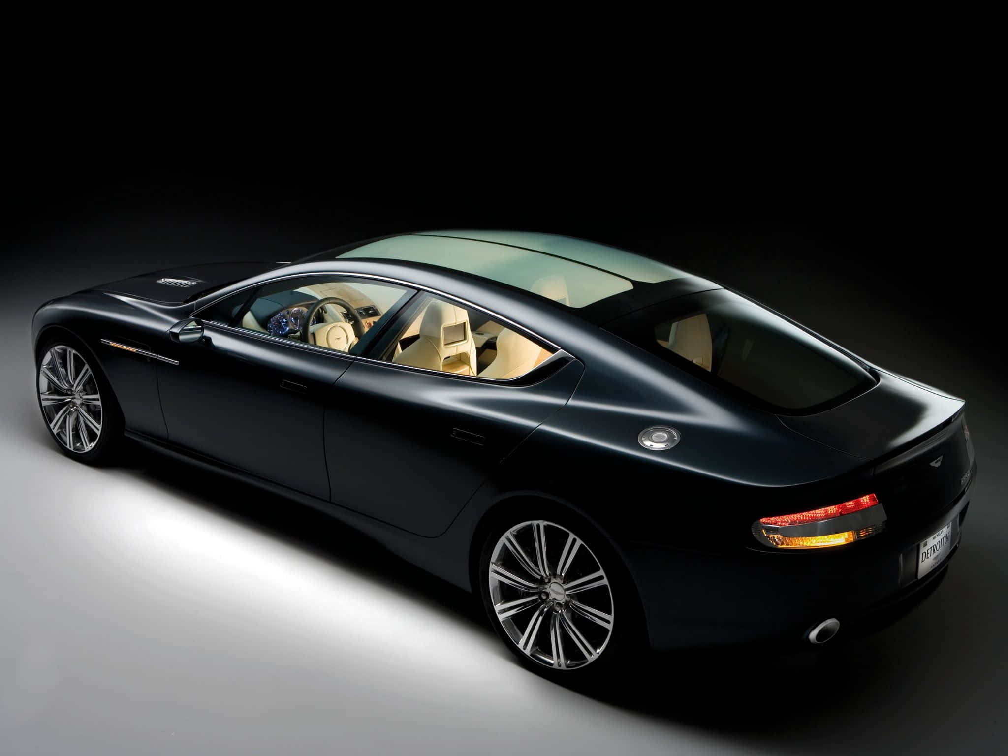 Aston Martin Rapide S 桌布 壁紙 — 一輛時尚的黑色豪華轎車，配以奶油色內裝，在深色背景的攝影棚燈光下閃耀。