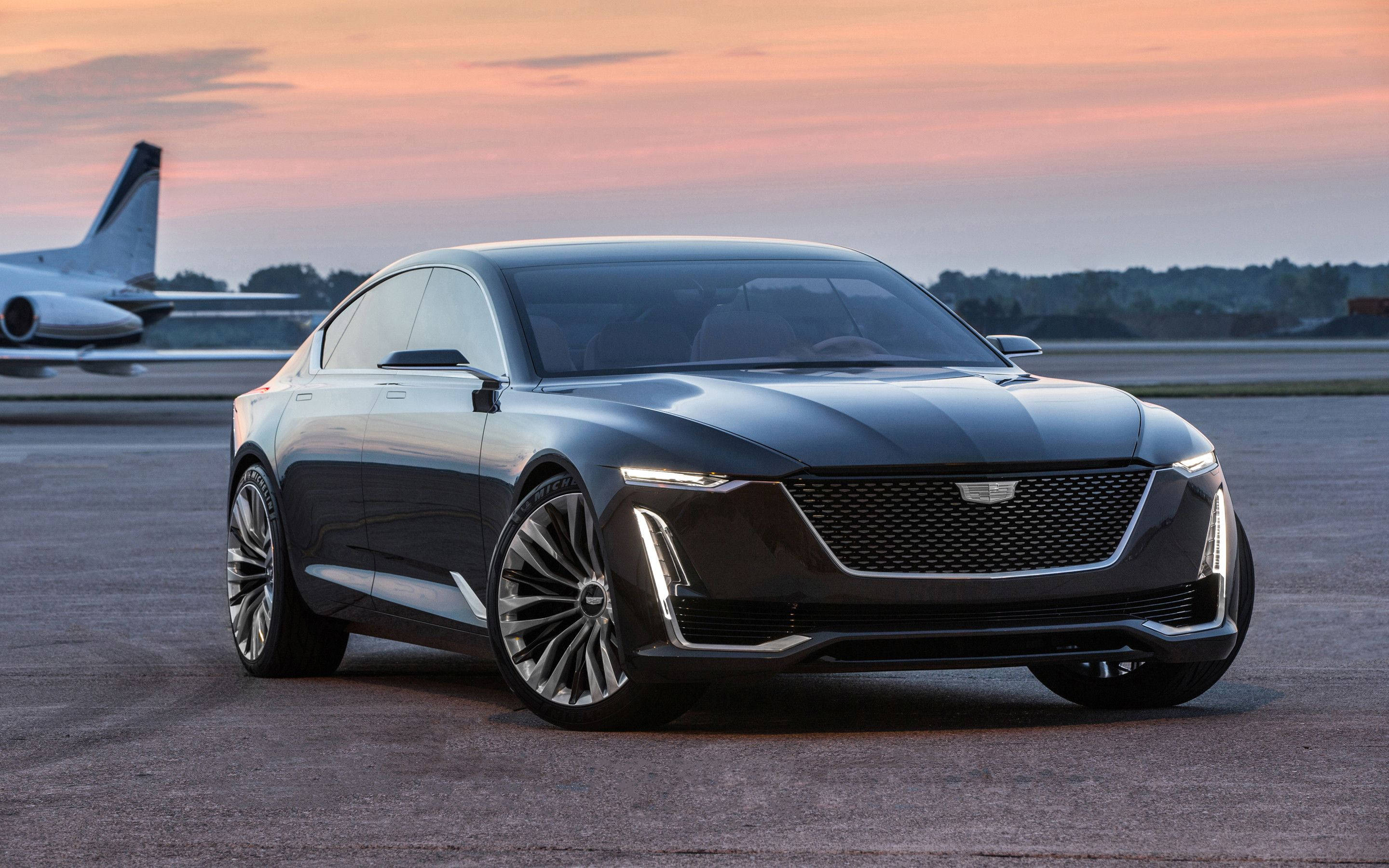 Cadillac 桌布 壁紙 — 一輛時尚的黑色豪華轎車在機場停機坪上閃閃發光，背景是日落和私人飛機。