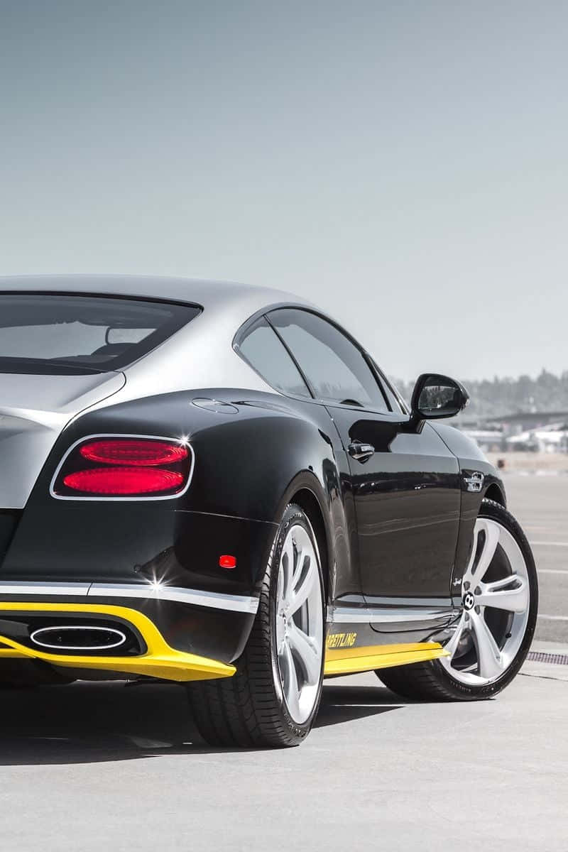bentley HD 桌布 壁紙 — 一輛時尚的黑色賓利 Continental GT 帶有醒目的黃色點綴，在明亮的日光下在鋪砌的路面上閃閃發光。