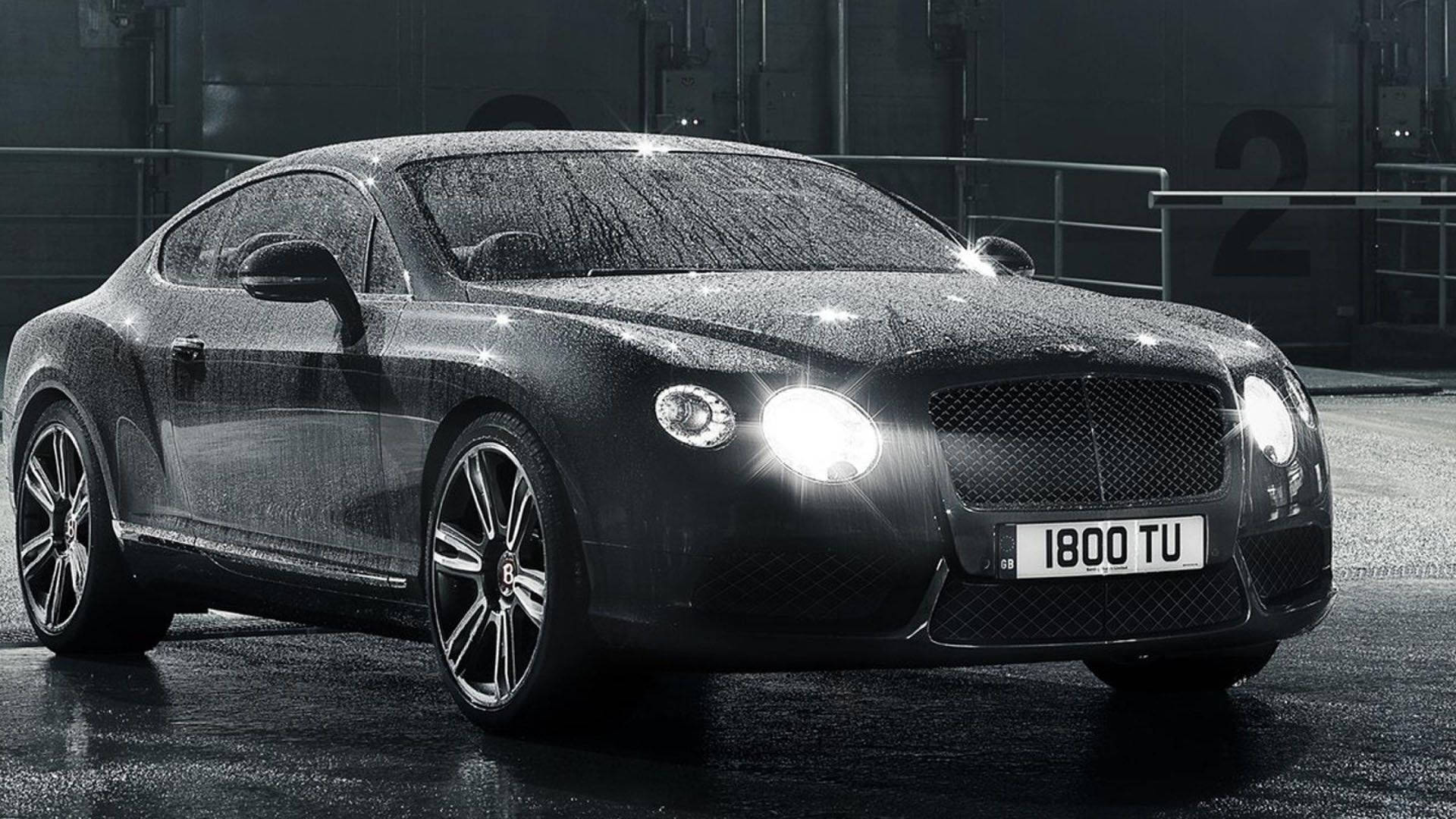 Raining 桌布 壁紙 — 一輛時尚的黑色賓利 Continental GT 在夜間潮濕的城市街道上，在明亮的車頭燈下閃閃發光。