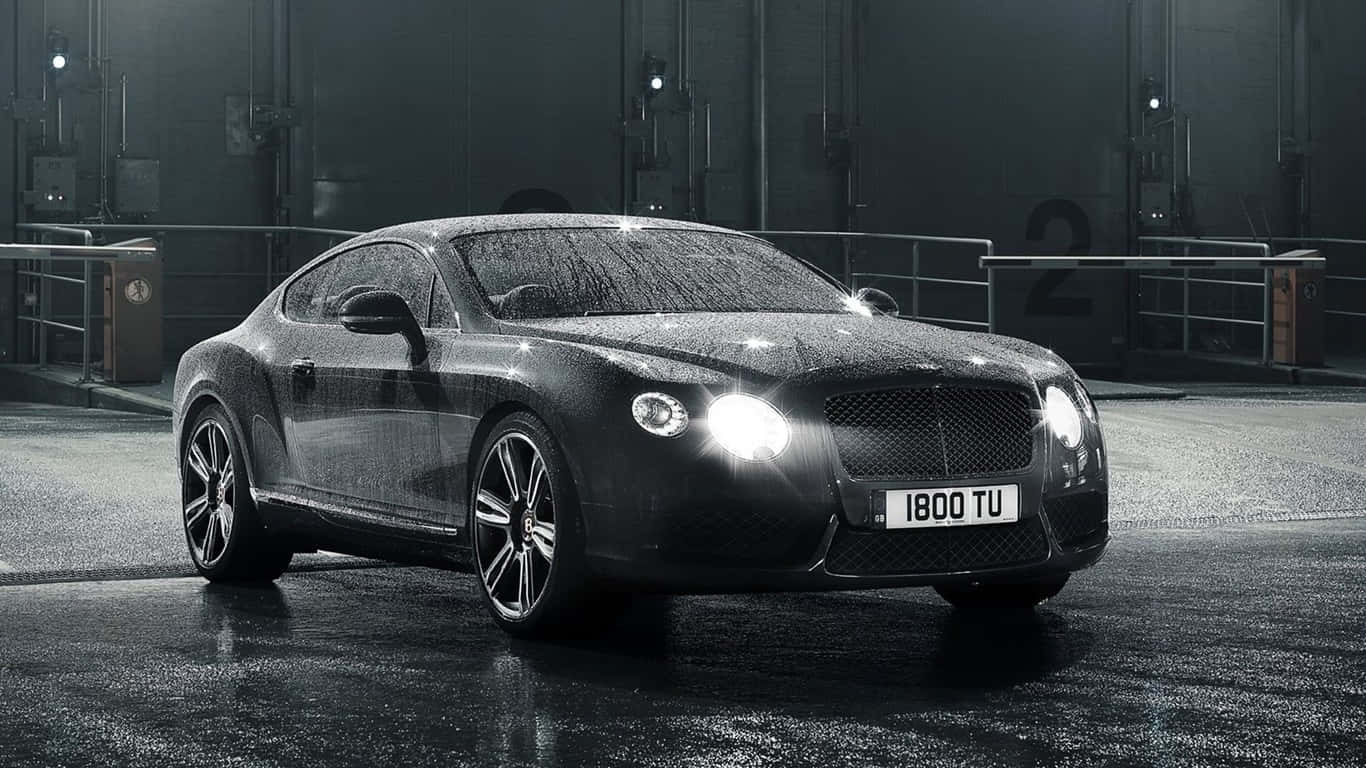 1366x768 Bentley 桌布 壁紙 — 一輛時尚的黑色賓利 Continental GT 在潮濕的工業車庫地板上，在明亮的車頭燈下閃閃發光。