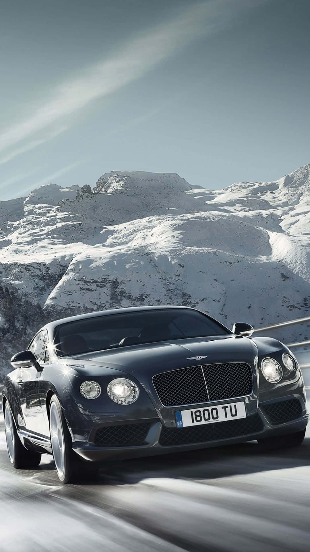 bentley HD 桌布 壁紙 — 一輛時尚的黑色賓利 Continental GT 在晴朗藍天下沿著積雪的山路飛馳。
