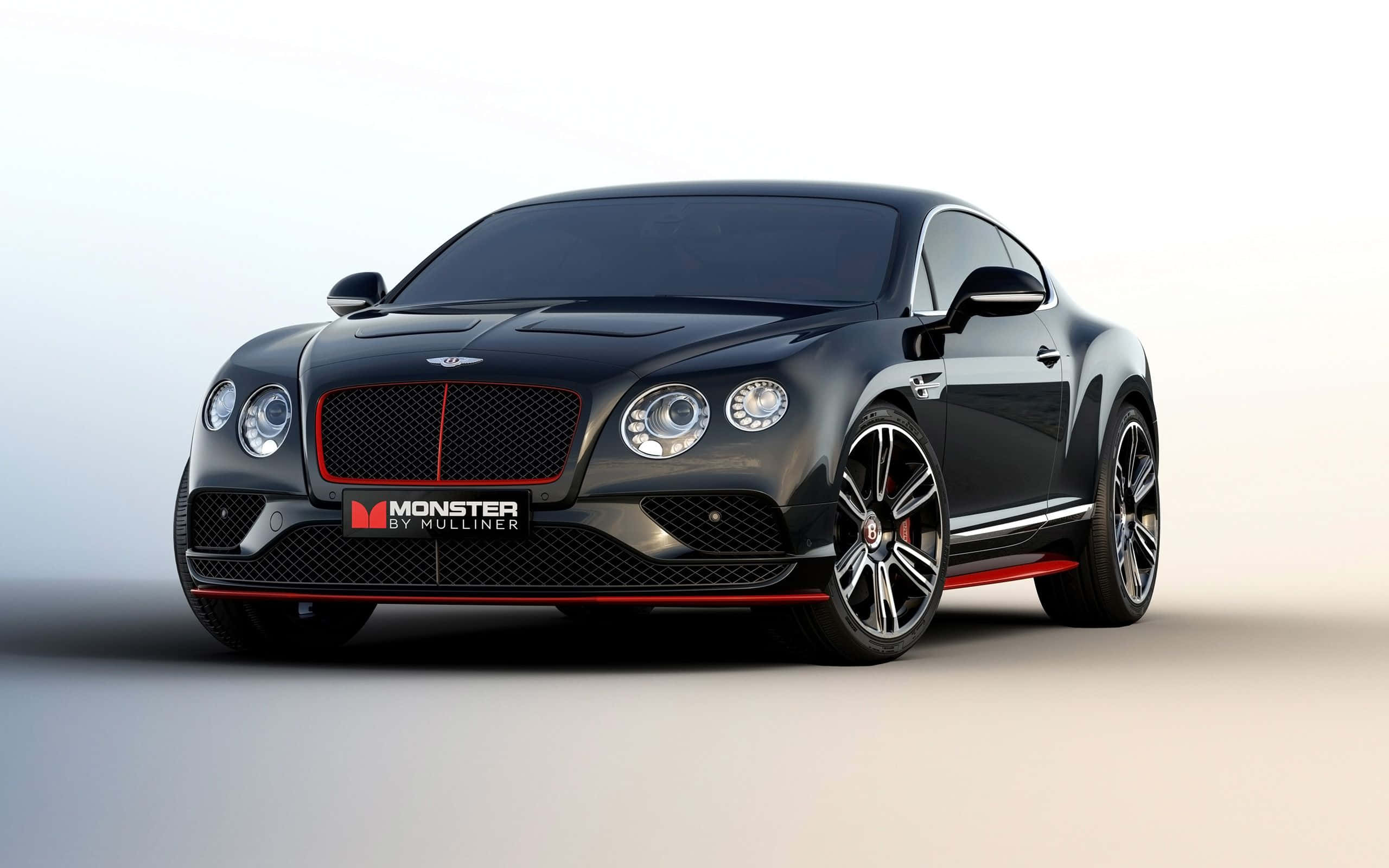 Best Bentley 桌布 壁紙 — 一輛時尚的黑色賓利 Continental GT，帶有紅色點綴和 'Monster by Mulliner' 徽章，置於簡約白色工作室背景前。