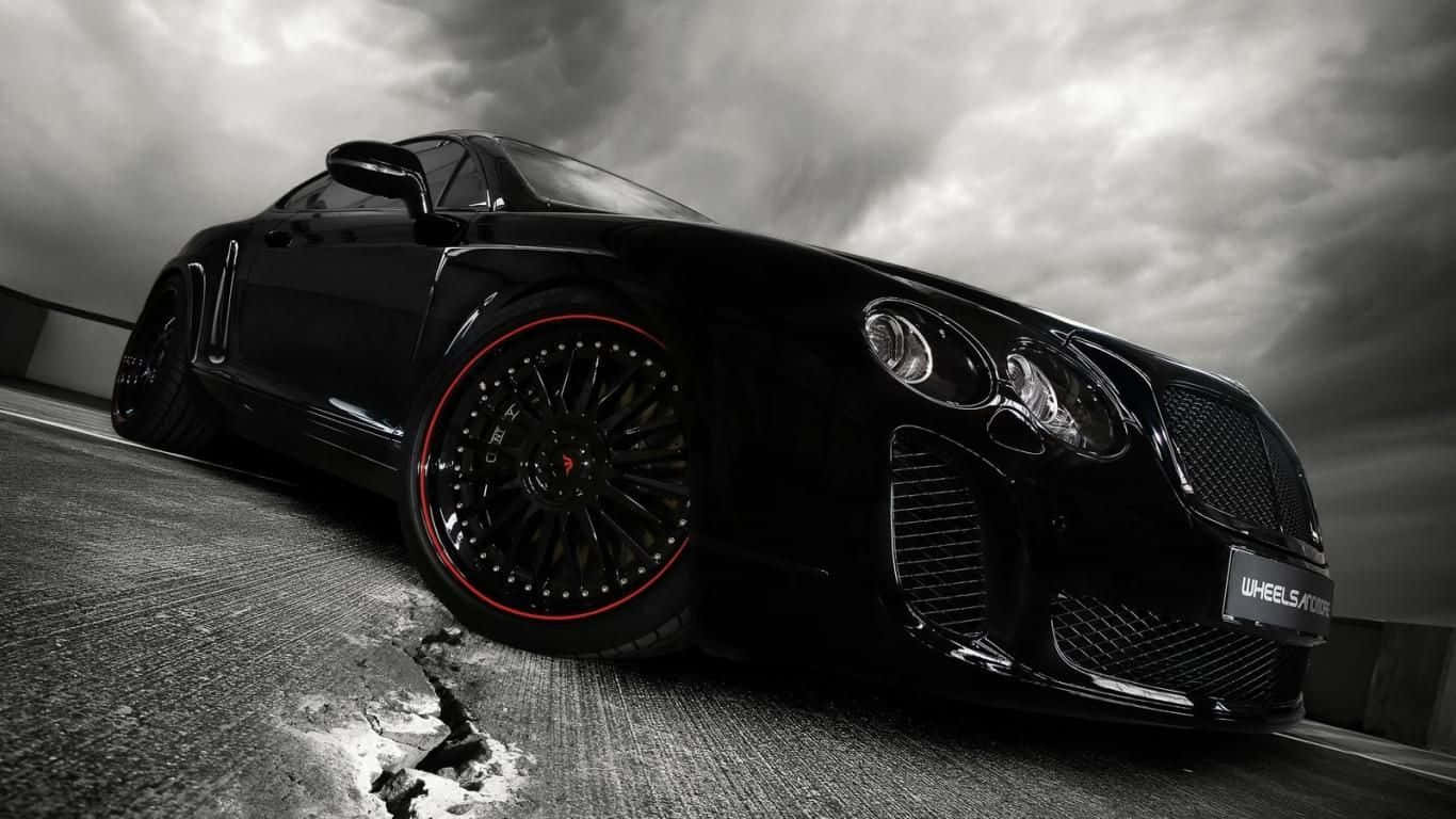 Best Bentley 桌布 壁紙 — 一輛時尚的黑色賓利 Continental GT 配備紅色輪圈，在戲劇性的雲層下主宰著暴風雨般的灰色瀝青道路。