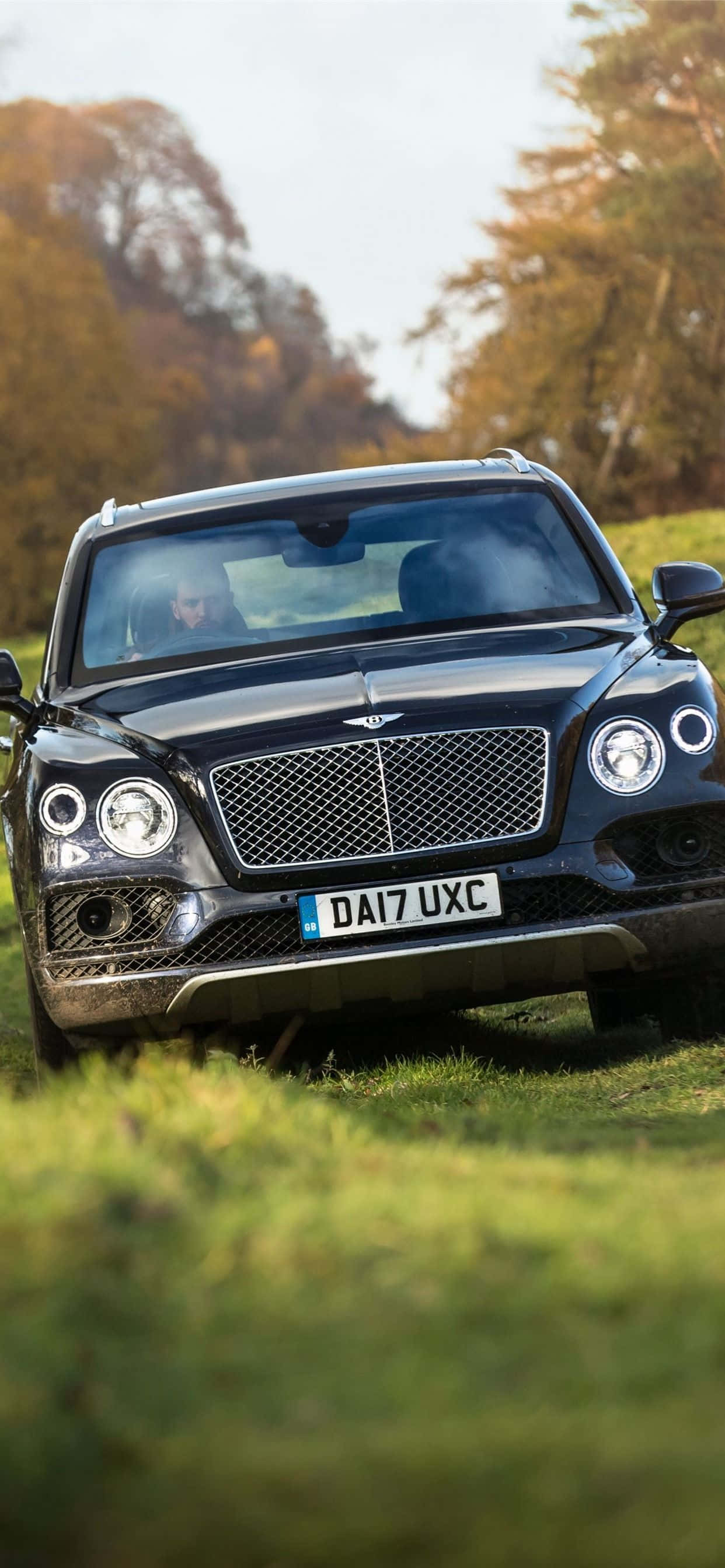 iPhone Xs Max Bentley 桌布 壁紙 — 一輛時尚的黑色賓利Bentayga SUV停在草地上，背景是秋天的樹木。