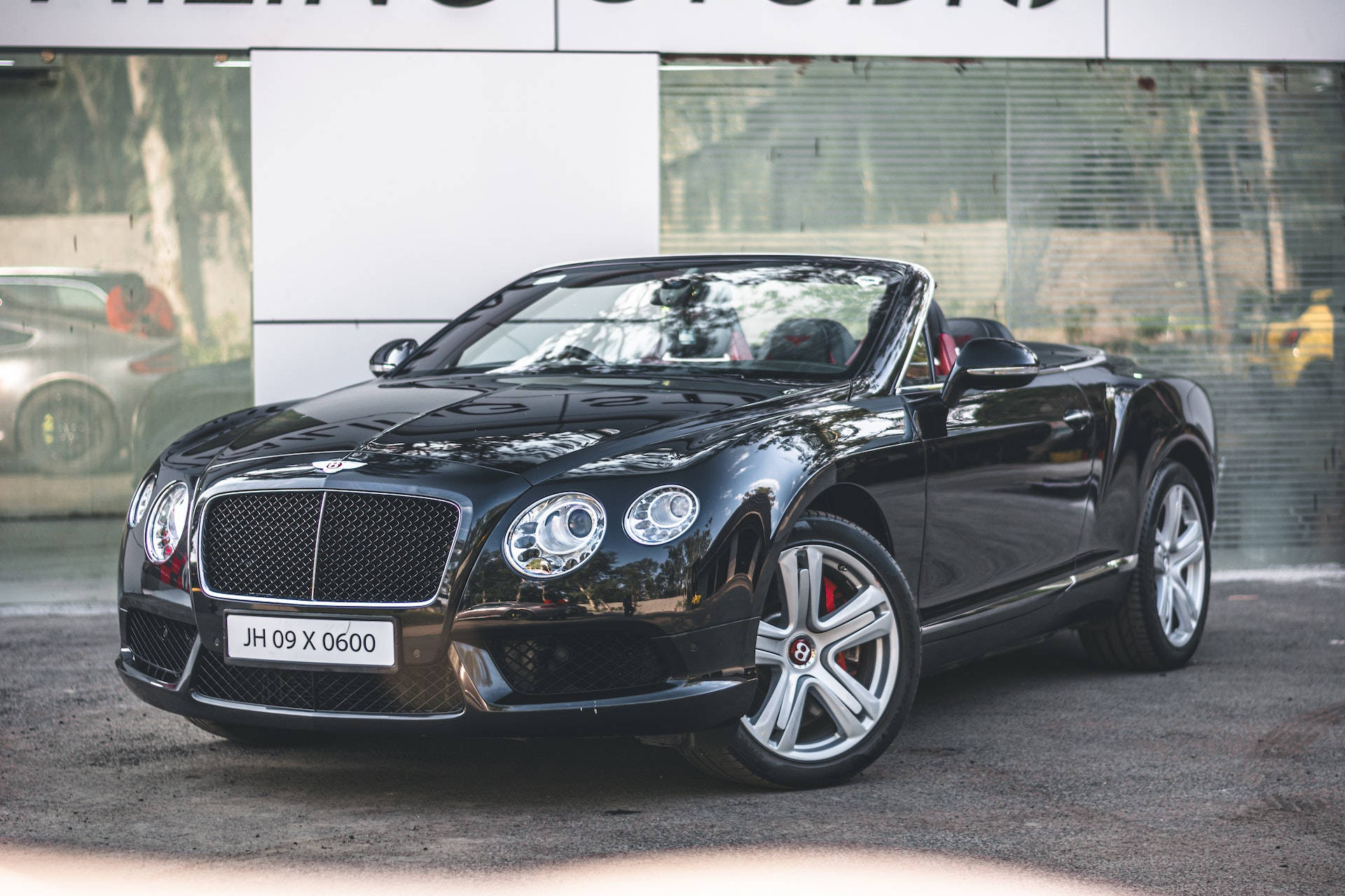 bentley HD 桌布 壁紙 — 一輛時尚的黑色賓利敞篷車停放在經銷商門外，鍍鉻飾邊和紅色制動卡鉗在日光下閃閃發光。