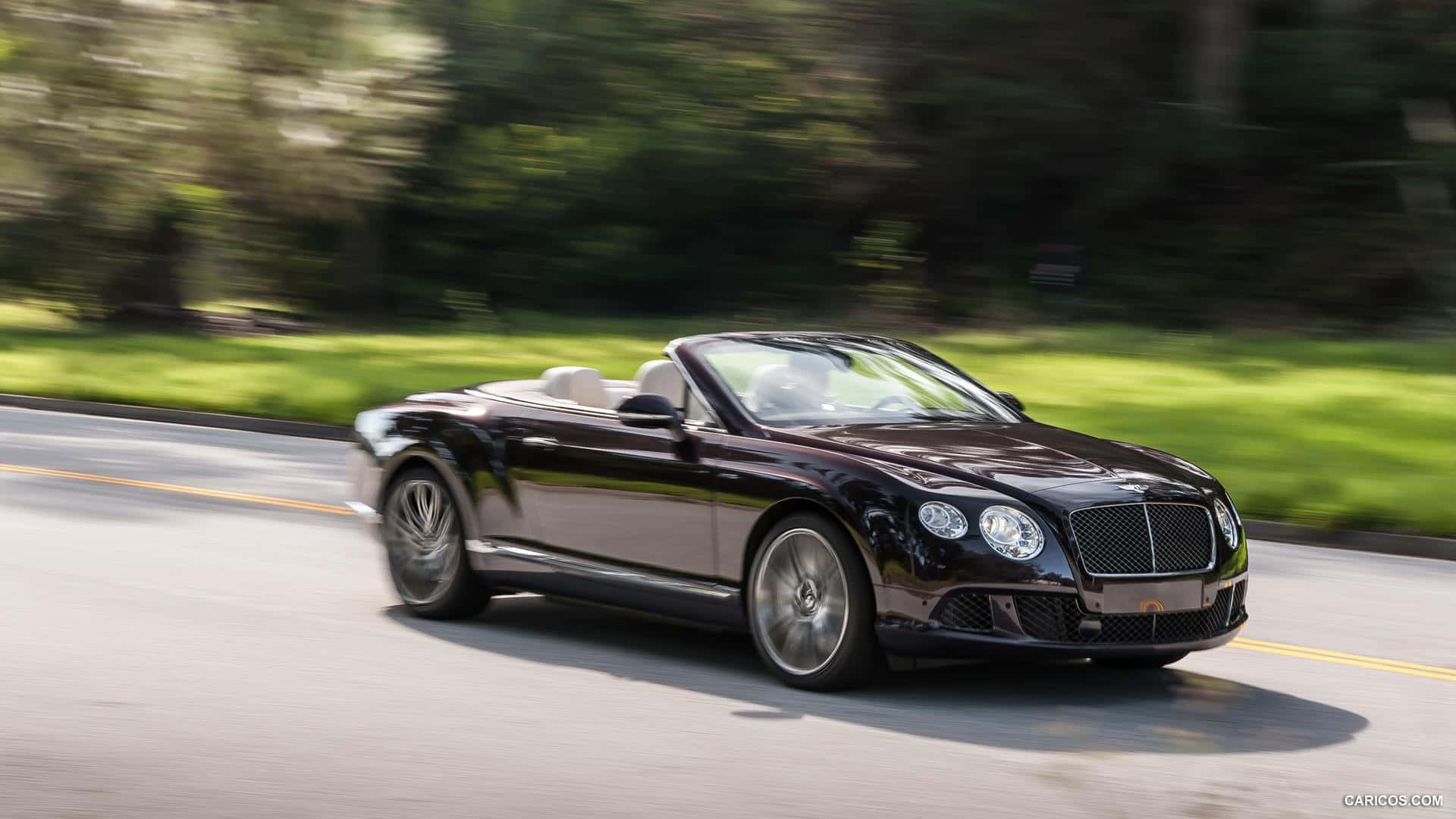 Convertible 桌布 壁紙 — 一輛時尚的黑色賓利敞篷車在陽光明媚的道路上行駛，背景是模糊的綠色樹木。