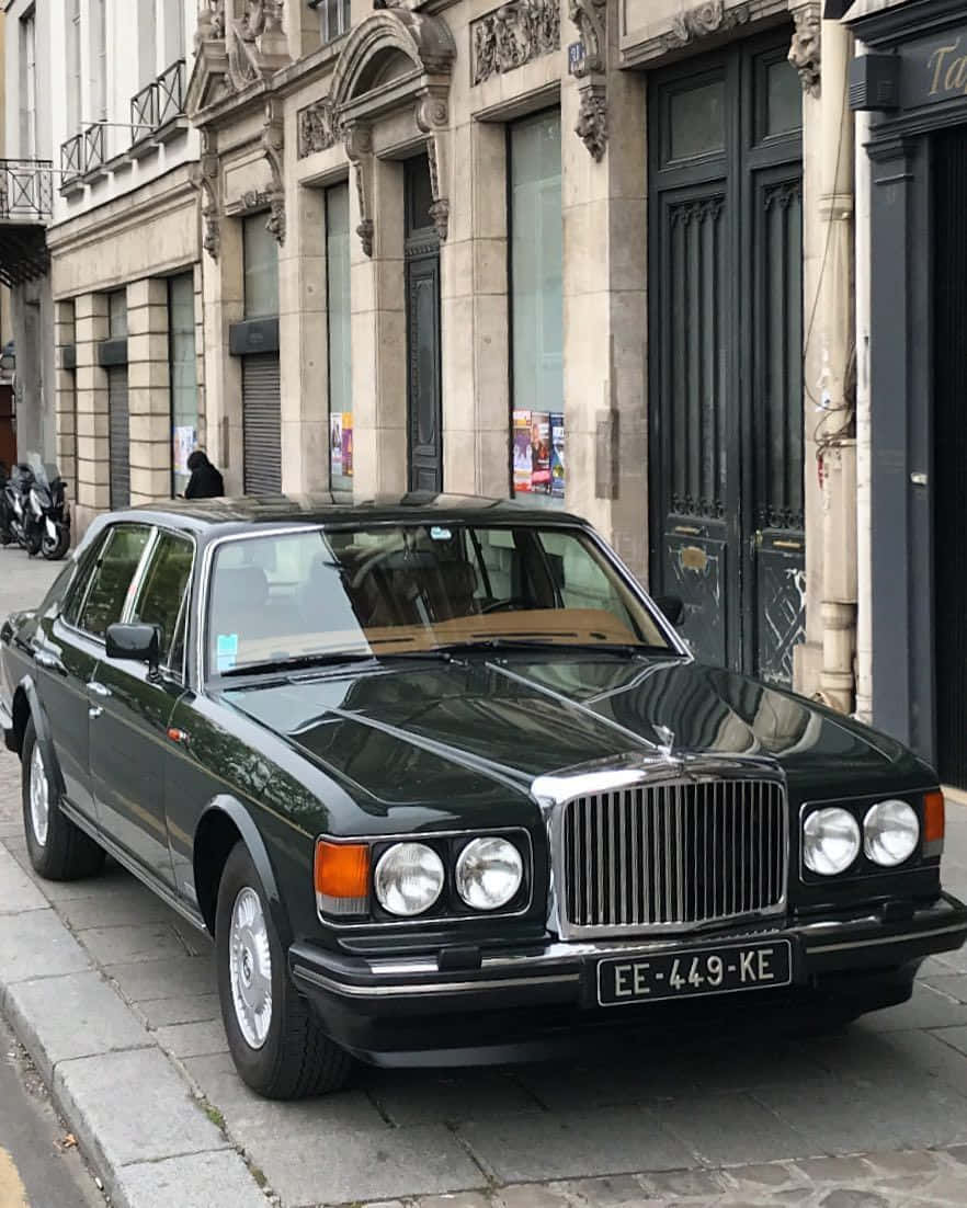 Bentley Eight 桌布 壁紙 — 一輛時尚的黑色賓利轎車停在鵝卵石街道上，旁邊是裝飾華麗的石造建築，帶有深色門。