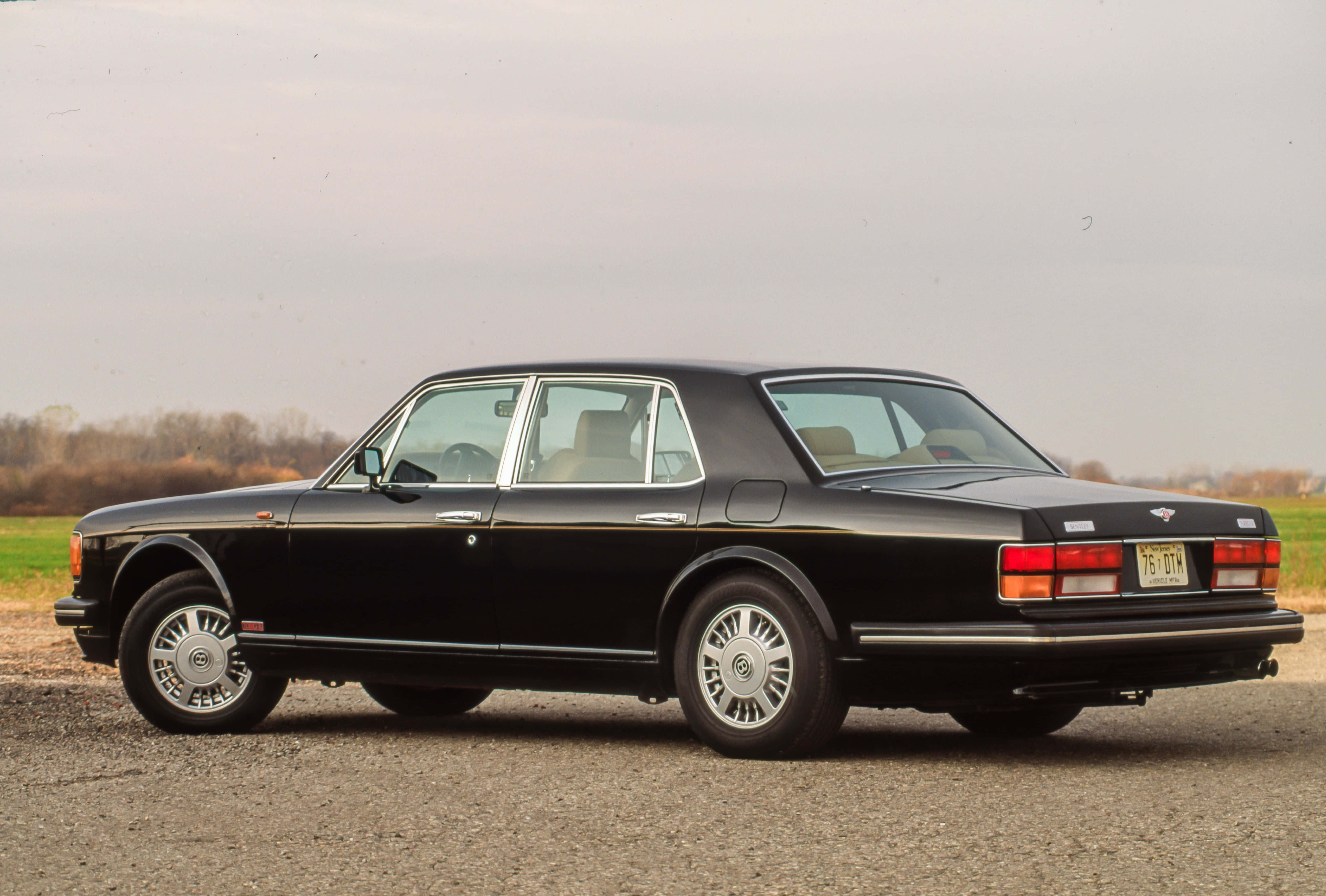 Bentley Turbo R 桌布 壁紙 — 一輛時尚的黑色賓利轎車停泊在碎石上，背景是柔和天空和光禿禿的樹木。