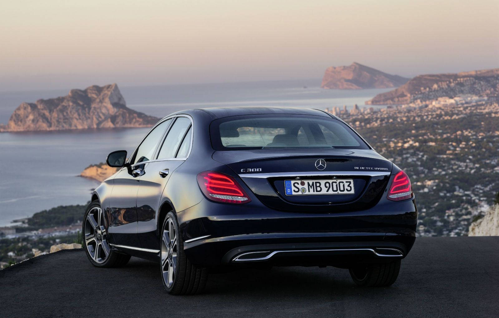 Mercedes Benz C300 桌布 壁紙 — 一輛時尚的黑色賓士E-Class轎車停泊在海岸懸崖上，俯瞰日落時分的城市與大海。