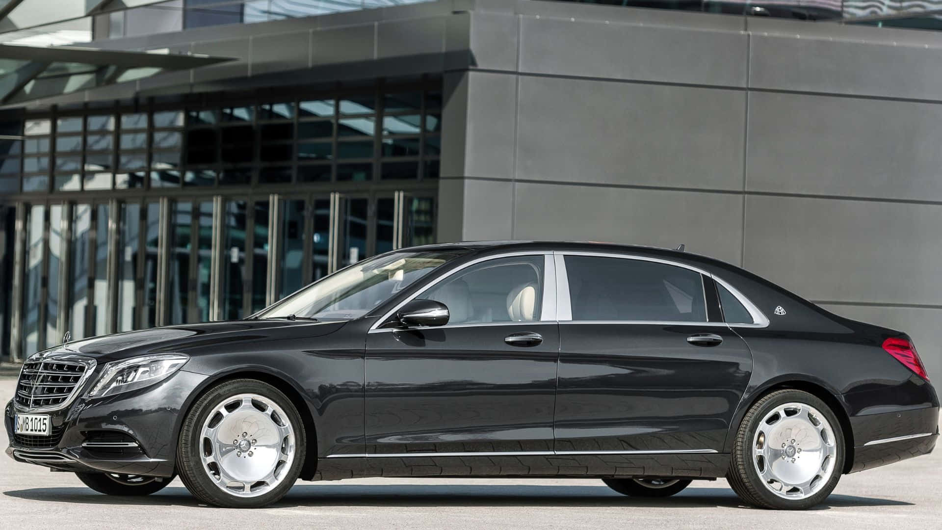 Maybach 桌布 壁紙 — 一輛時尚的黑色賓士S-Class轎車停在現代玻璃及鋼結構建築物前，在明亮的日光下。