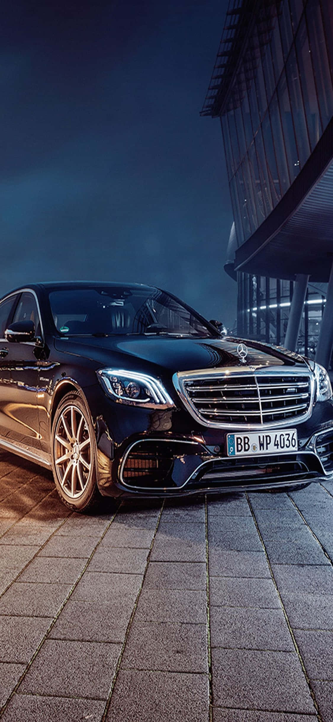Mercedes 桌布 壁紙 — 一輛時尚的黑色賓士S-Class轎車在夜燈下閃閃發光，旁邊是一座現代玻璃建築，位於鋪砌的廣場上。