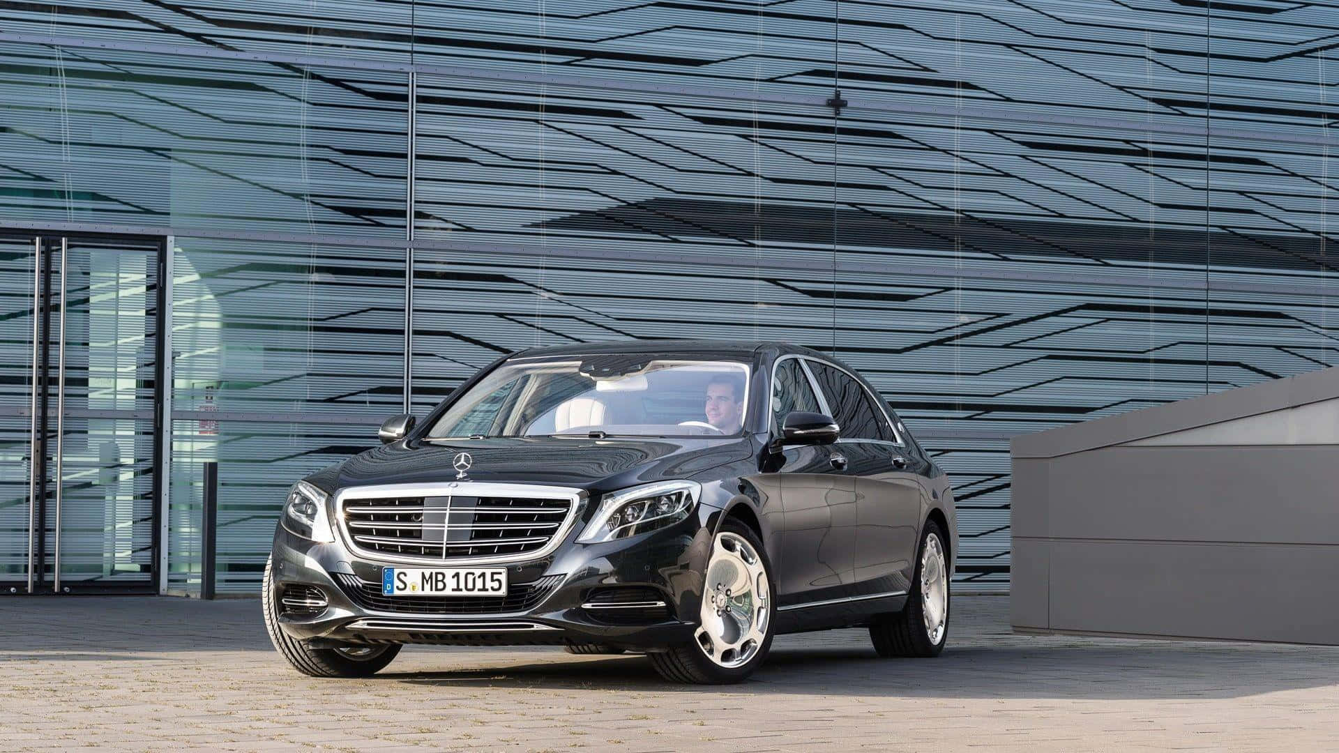Maybach 桌布 壁紙 — 一輛時尚的黑色賓士S-Class轎車停在現代幾何圖案玻璃建築前。