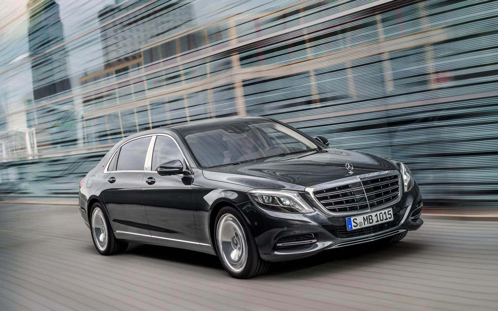 Maybach 桌布 壁紙 — 一輛時尚的黑色賓士S-Class轎車在現代城市景觀中疾馳，背景是模糊的玻璃建築。