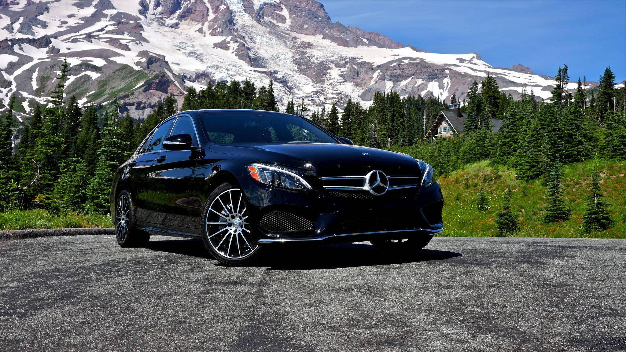 Mercedes Benz C300 桌布 壁紙 — 一輛時尚的黑色賓士轎車停在柏油路上，背景是白雪覆蓋的山脈和常綠樹木，天空清澈湛藍。
