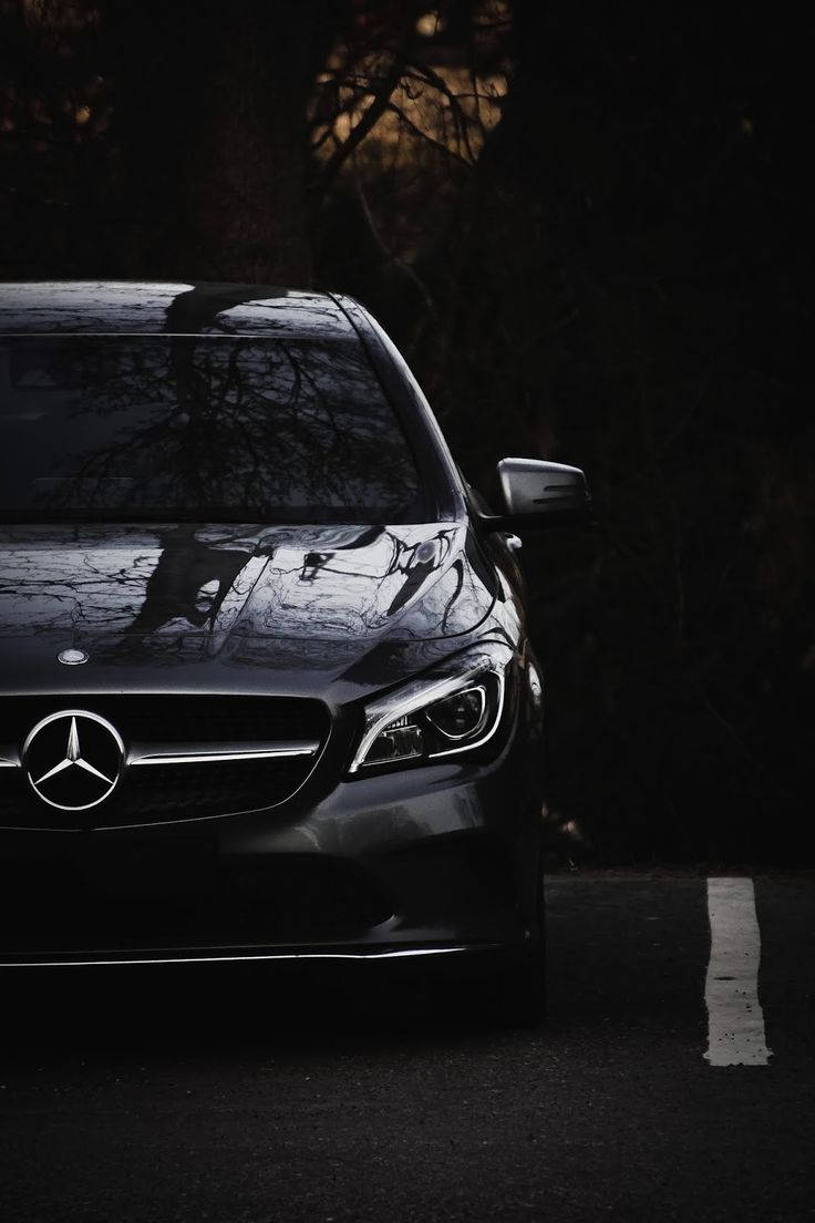 Mercedes 桌布 壁紙 — 一輛時尚的黑色賓士轎車停在燈光昏暗的道路上，樹木的倒影在光亮的引擎蓋上閃爍。