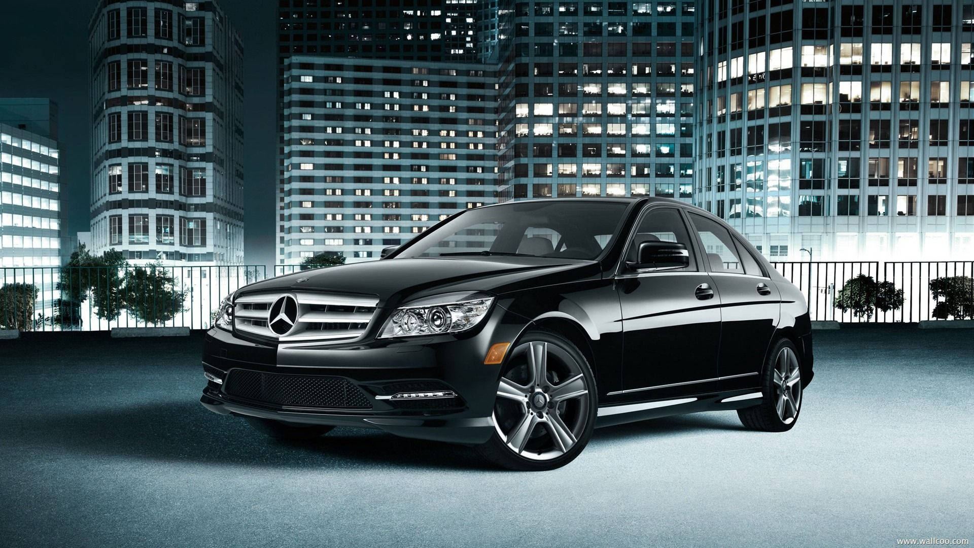Mercedes Benz C300 桌布 壁紙 — 一輛時尚的黑色賓士轎車在夜晚的城市燈光下，以燈火通明的摩天大樓為背景閃閃發光。