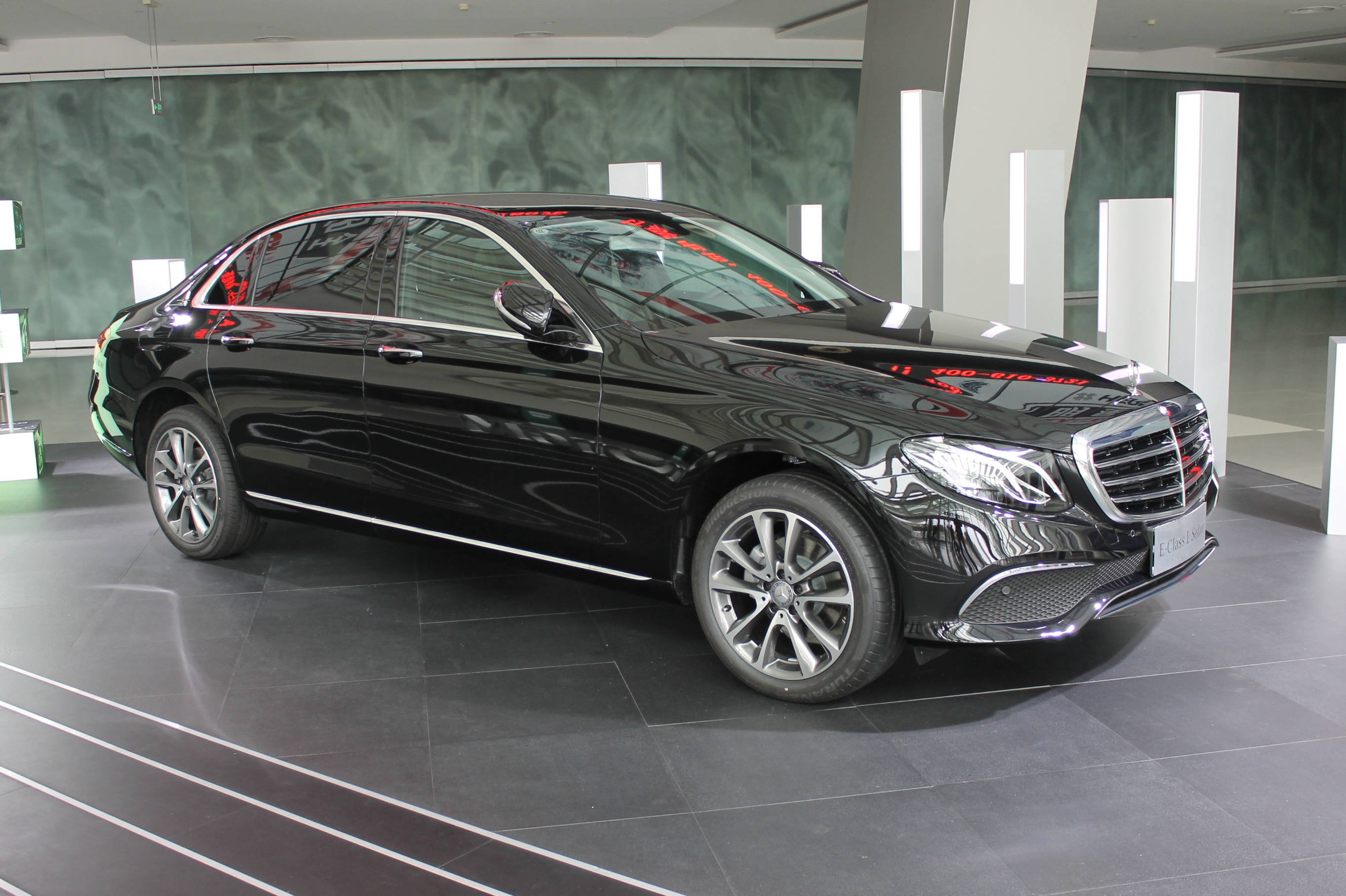 Mercedes 桌布 壁紙 — 一輛時尚的黑色賓士轎車在明亮的燈光下，於現代簡約的展示間中閃耀，展示間設有灰色瓷磚地板和綠色大理石牆壁。