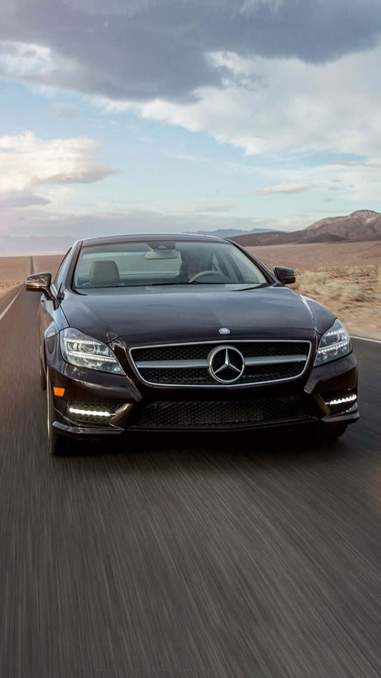 Mercedes 桌布 壁紙 — 一輛時尚的黑色賓士轎車在沙漠高速公路上奔馳，天空多雲，遠處有山巒。