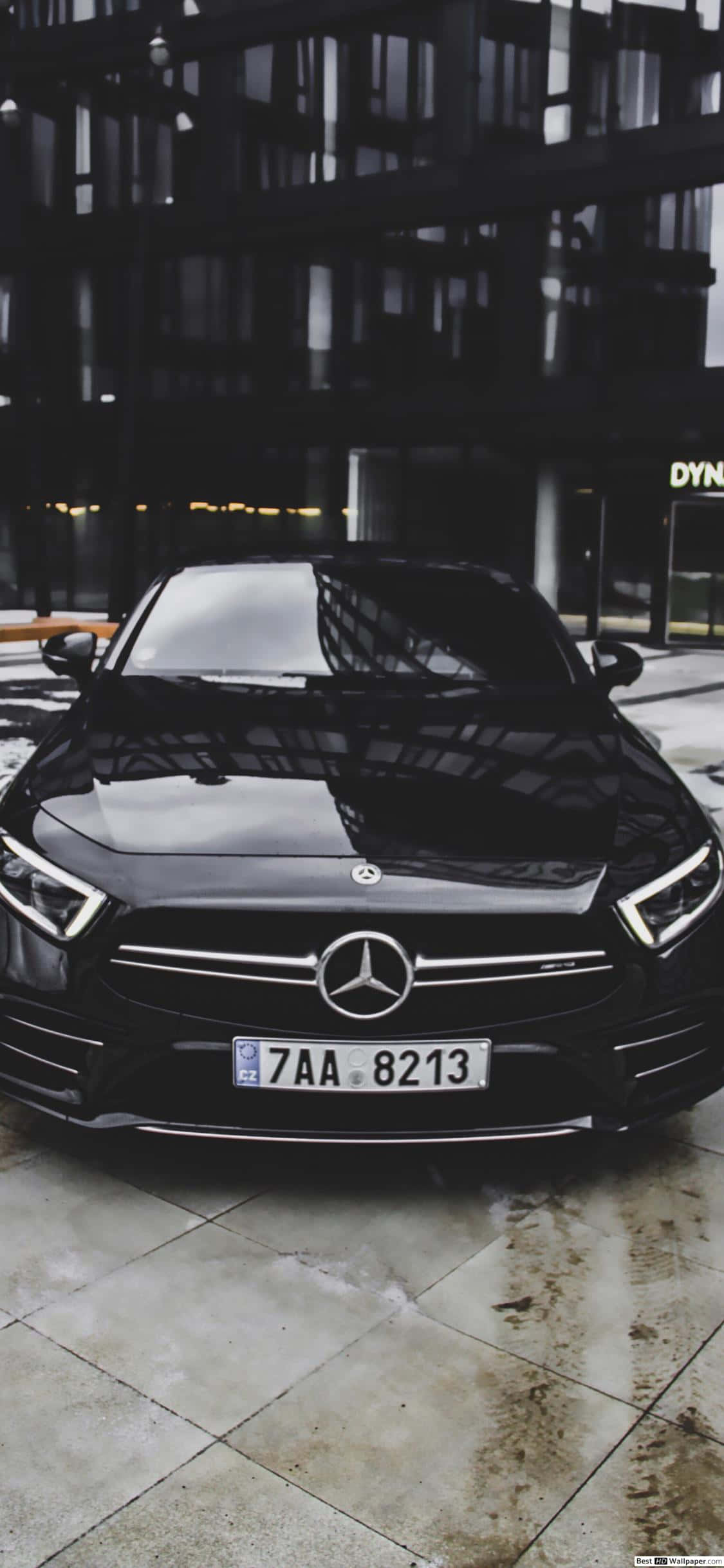 Mercedes 桌布 壁紙 — 一輛時尚的黑色賓士轎車在濕滑的瓷磚街道上，於城市燈光下閃閃發光，背後是現代建築。