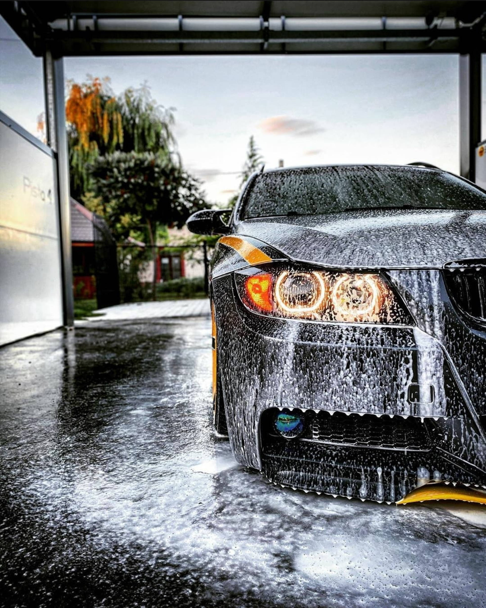 Wash 桌布 壁紙 — 一輛時尚的黑色跑車，帶有發光的車頭燈，正在車庫門下清洗，水流過其濕潤的表面。