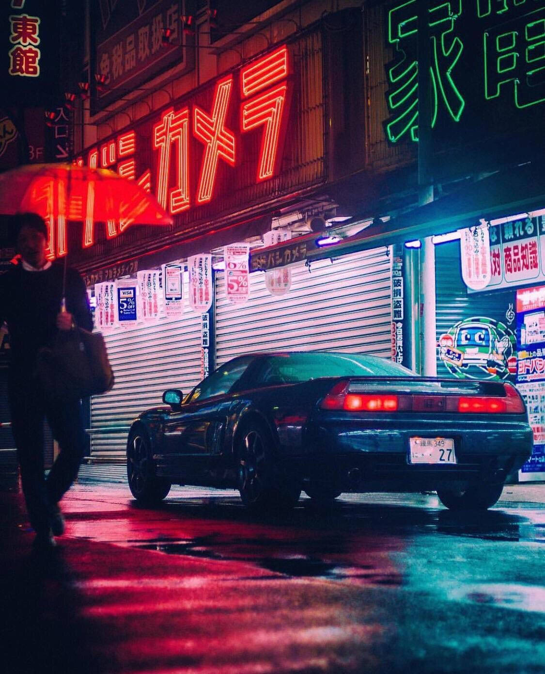 JDM汽車 桌布 壁紙 — 一輛時尚的黑色跑車停在夜晚霓虹燈閃爍的東京雨街上，一名行人手持紅色雨傘。