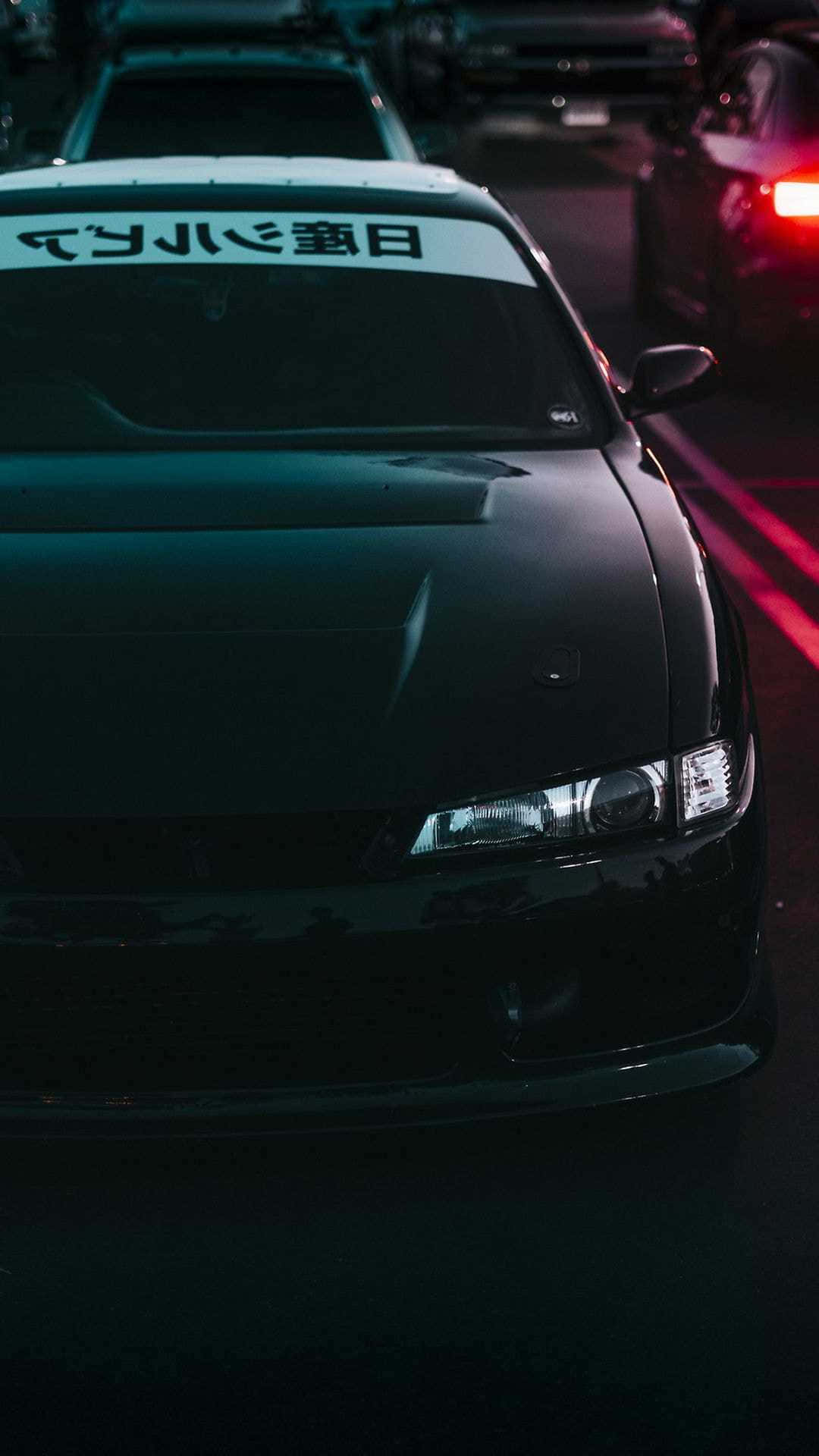 JDM 桌布 壁紙 — 一輛時尚的黑色跑車在夜晚雨中的城市街道上，在霓虹燈下發光。